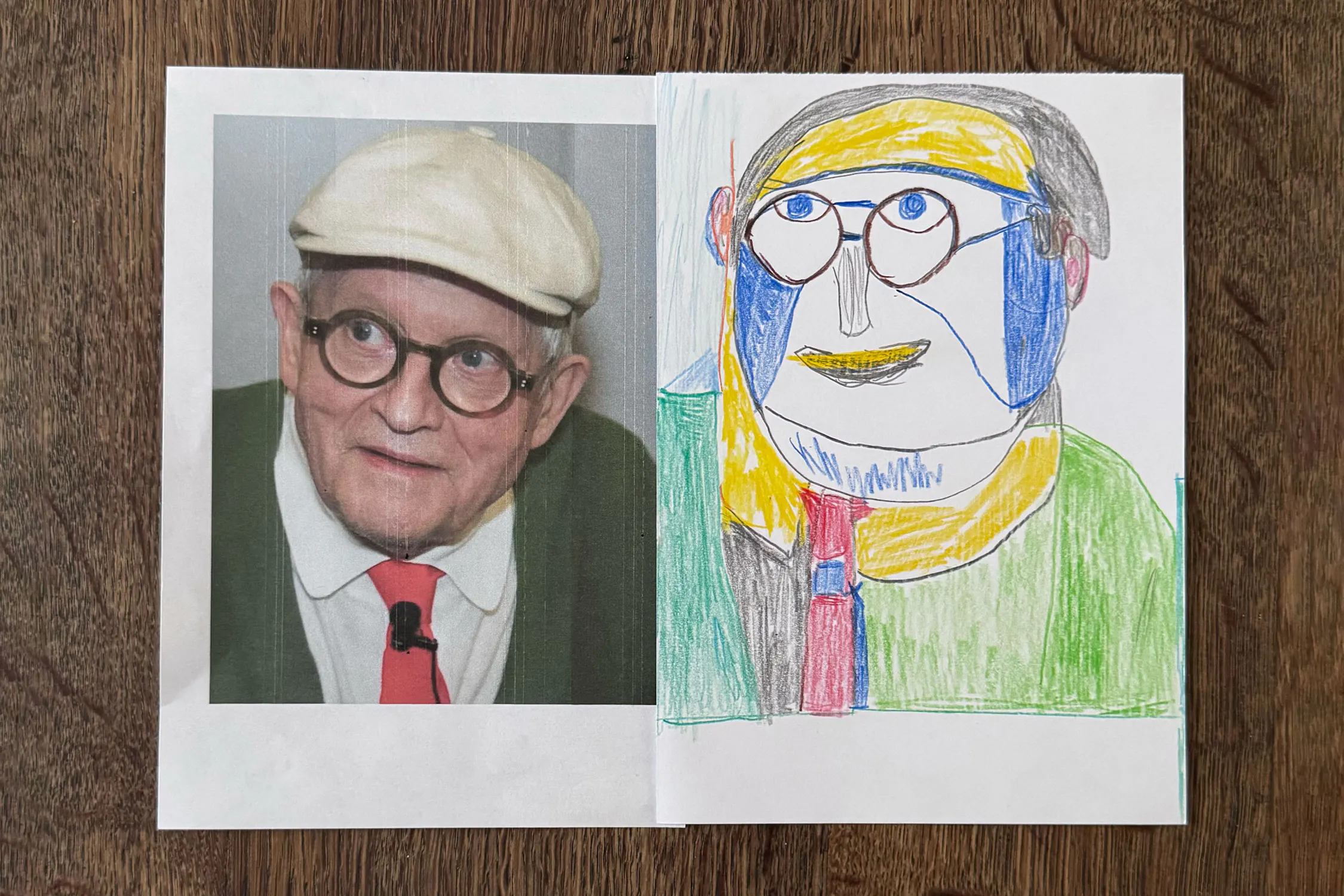 A photo of artist David Hockney, with glasses, a white cap, red tie, and green jumper, is on the left. On the right is a colourful, abstract crayon drawing by Christine Hazell of the same man, mimicking his features in a playful, childlike style. Both are on white paper.