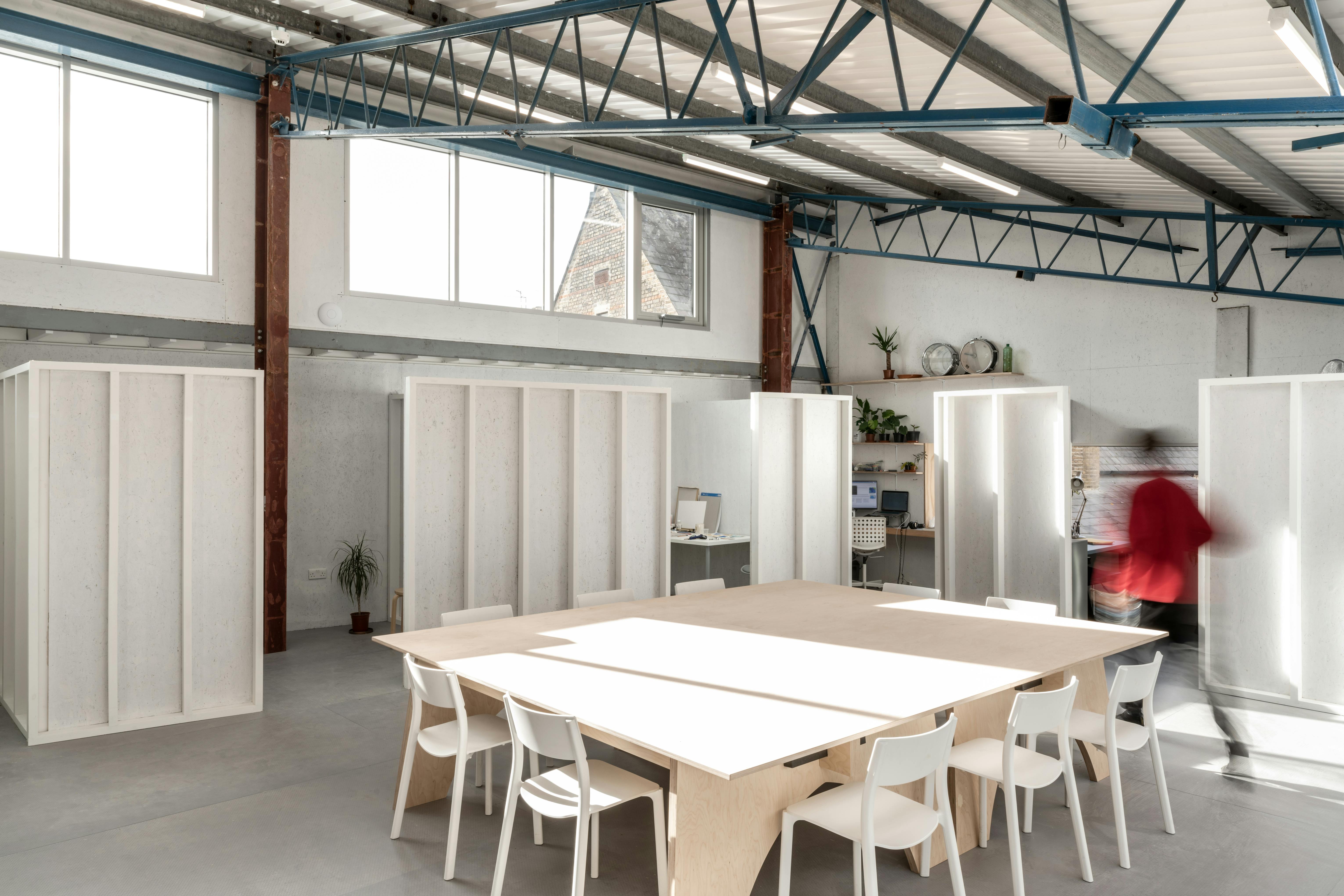 a long-exposure shot captures a person walking through Studio Voltaire's communal studio – a large space with a slanted rood, exposed steel beams and large ceiling windows.