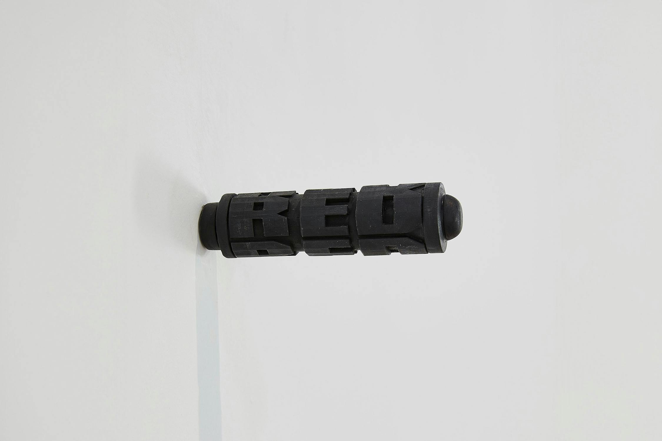 A black cylindrical object with raised block letters spelling "RED" protrudes horizontally from a white wall.