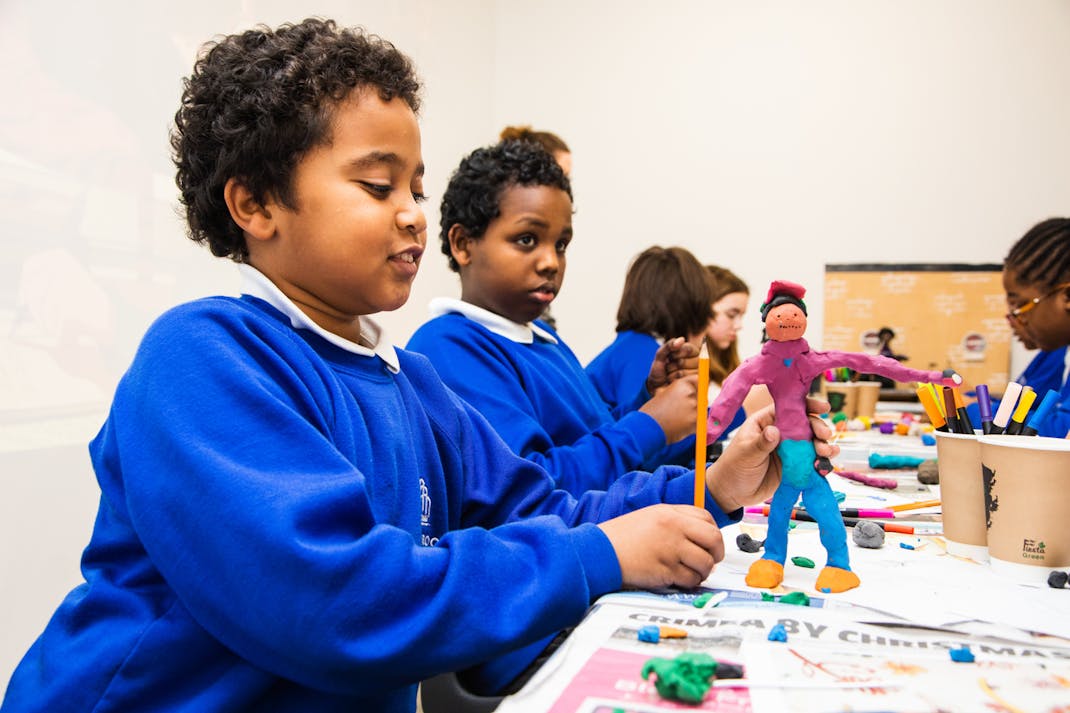 a school child wearing a blue uniform holds a plasticine figure made during a creative workshop