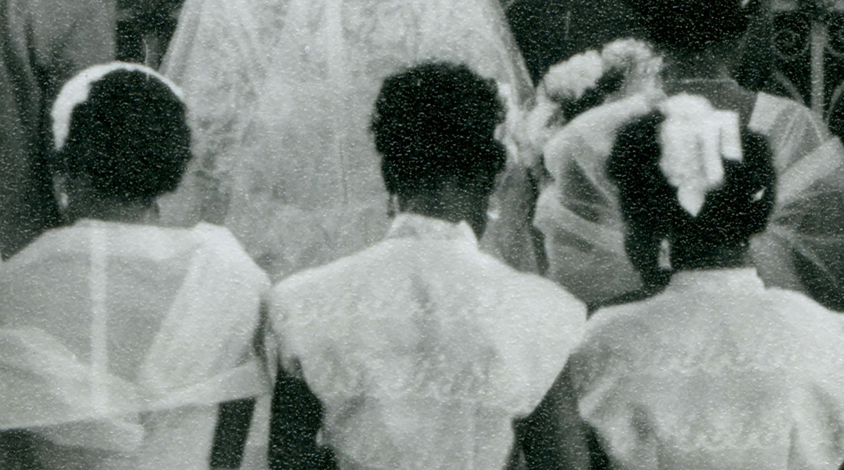 A vintage black and white photo showing three young flower girls with curly hair, wearing light-colored dresses with bows, walking behind a bride in a lacy veil and gown. The scene captures a traditional wedding ceremony.