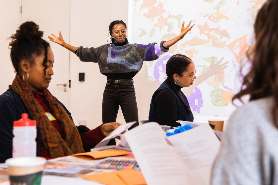 Artist Holly Graham stands with outstretched arms in front of a group of women participating in a workshop