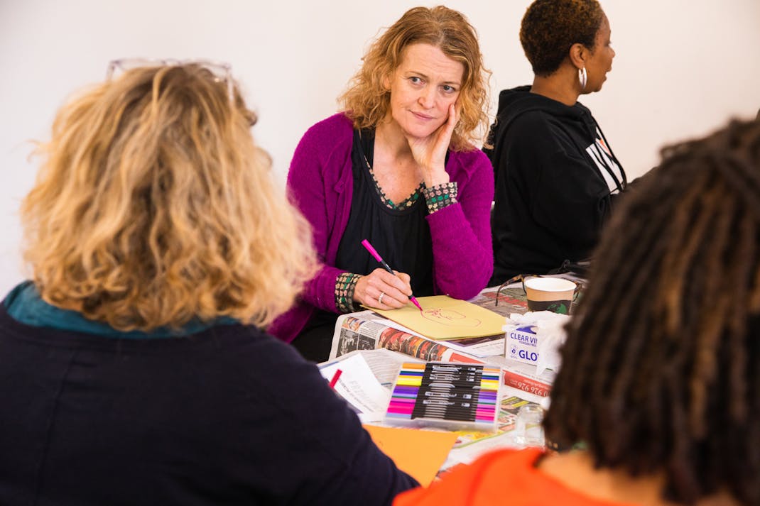 a white woman in a purple cardigan darws on yellow paper with felt-tip pens