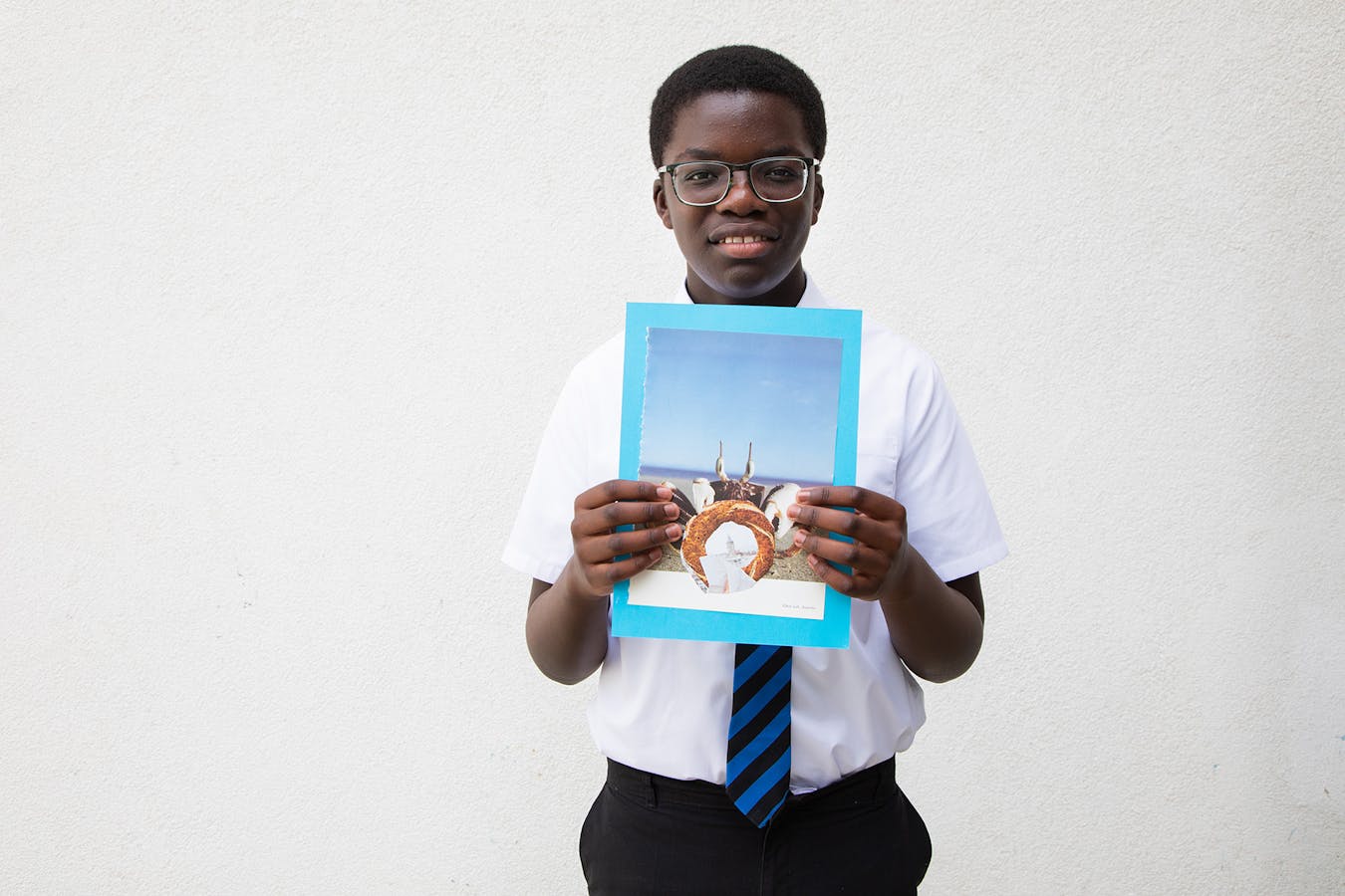 a young black schoolboy smiles and holds a collage made during a collage workshop
