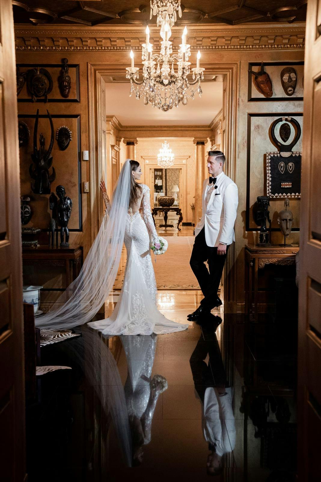 Bride and groom posing at their wedding venue with a beautiful chandelier glowing in the background.