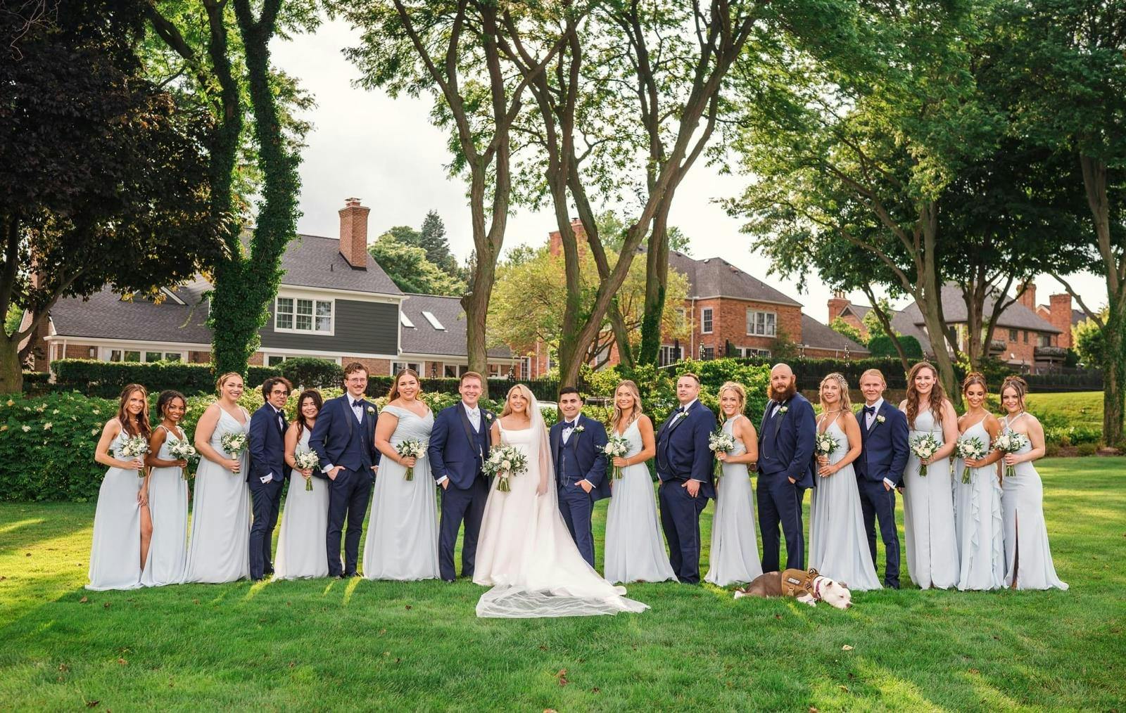 Wedding party standing together in nature, featuring the bride, groom, bridesmaids, and groomsmen.