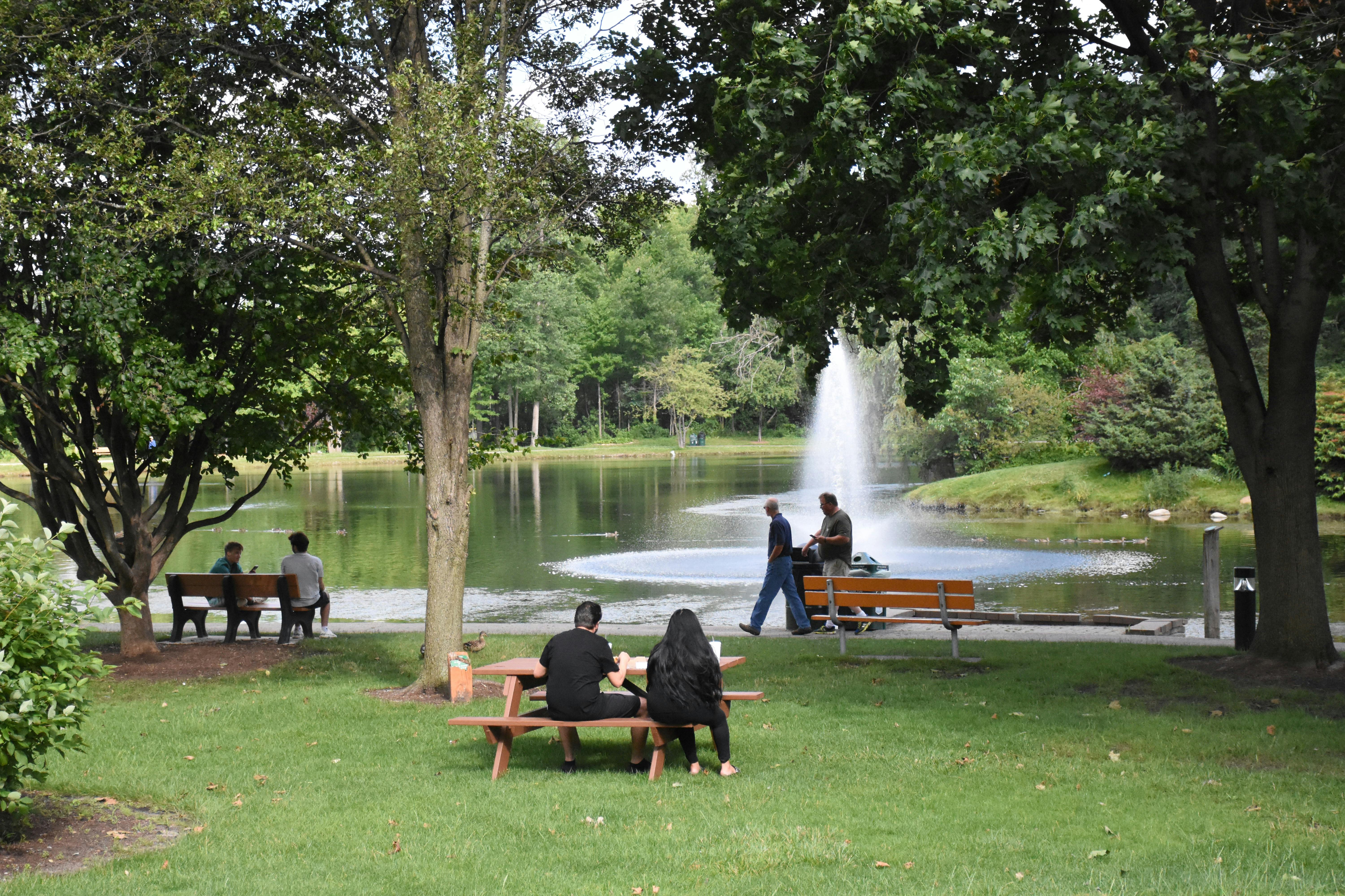 Visitors relaxing on a bench in a Shelby Township park, enjoying a clear view of the lake and the natural scenery.