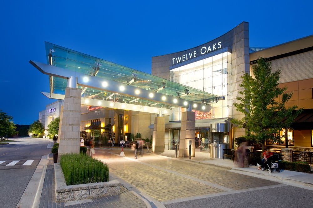 A spacious interior view of Twelve Oaks Mall in Novi, Michigan, showing multiple storefronts, open walkways, and shoppers exploring the modern retail environment.