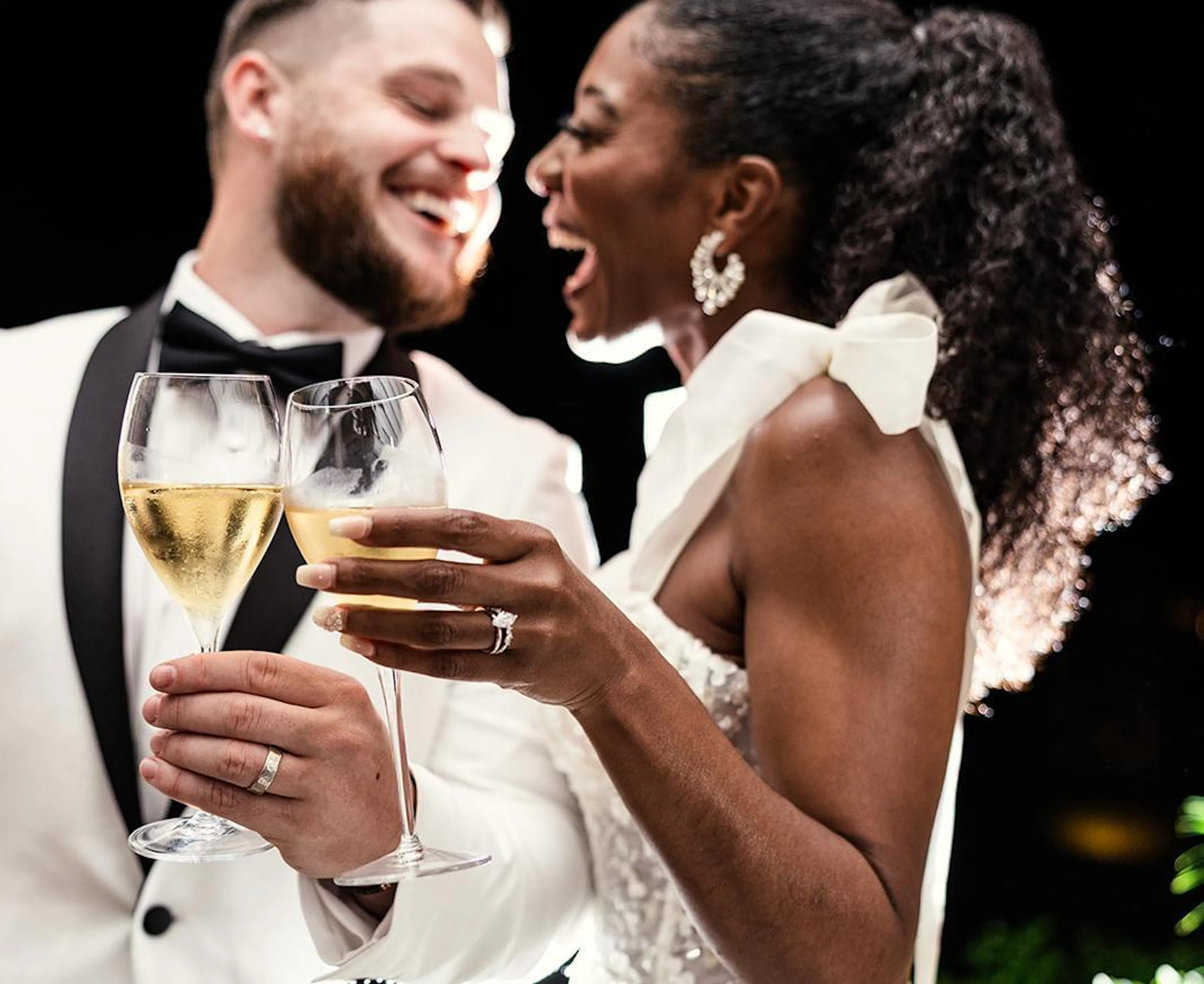 Newlywed couple in wedding attire toasting with champagne glasses and showing their wedding rings.