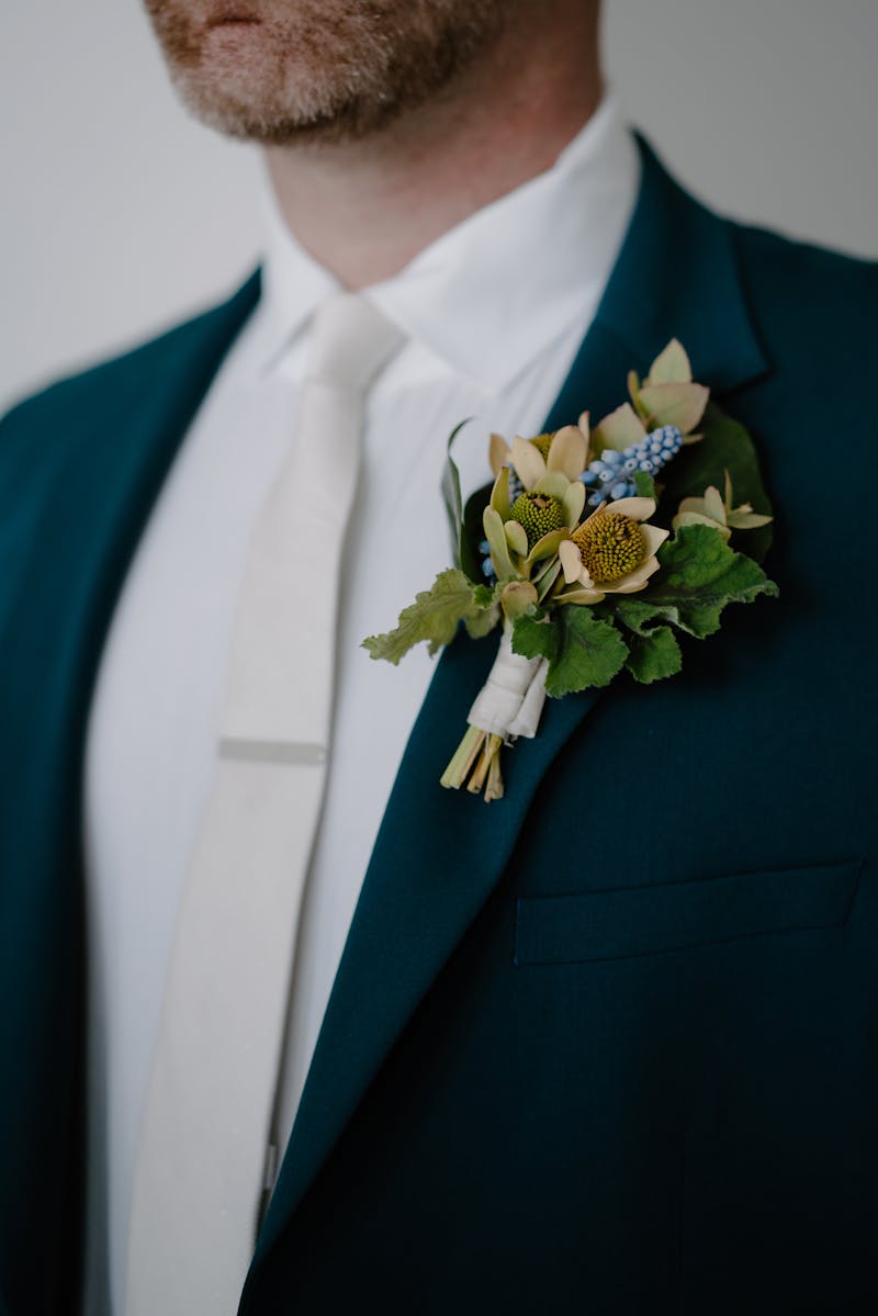 Greenhouse inspired yellow and blue boutonnière on a deep teal groom wedding suit