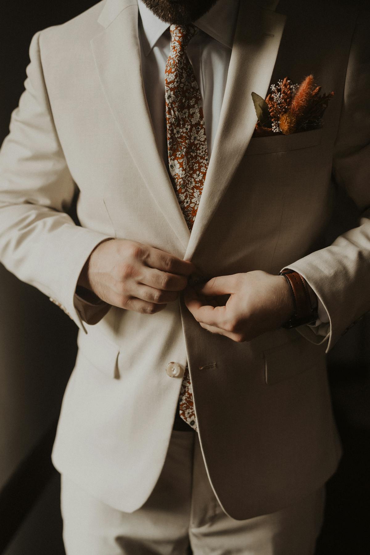 Tan wedding suit with rust orange floral tie and pocket boutonniere floral arrangement for groomsmen.