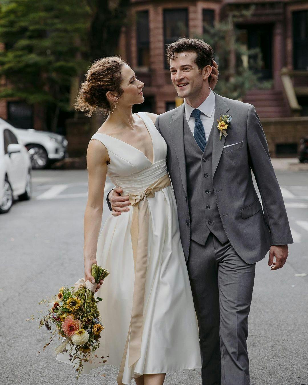 Brooklyn wedding with vintage bride style in midi wedding gown holding wildflower bouquet and groom in a light grey 3 piece suit with a sunflower boutonnière.