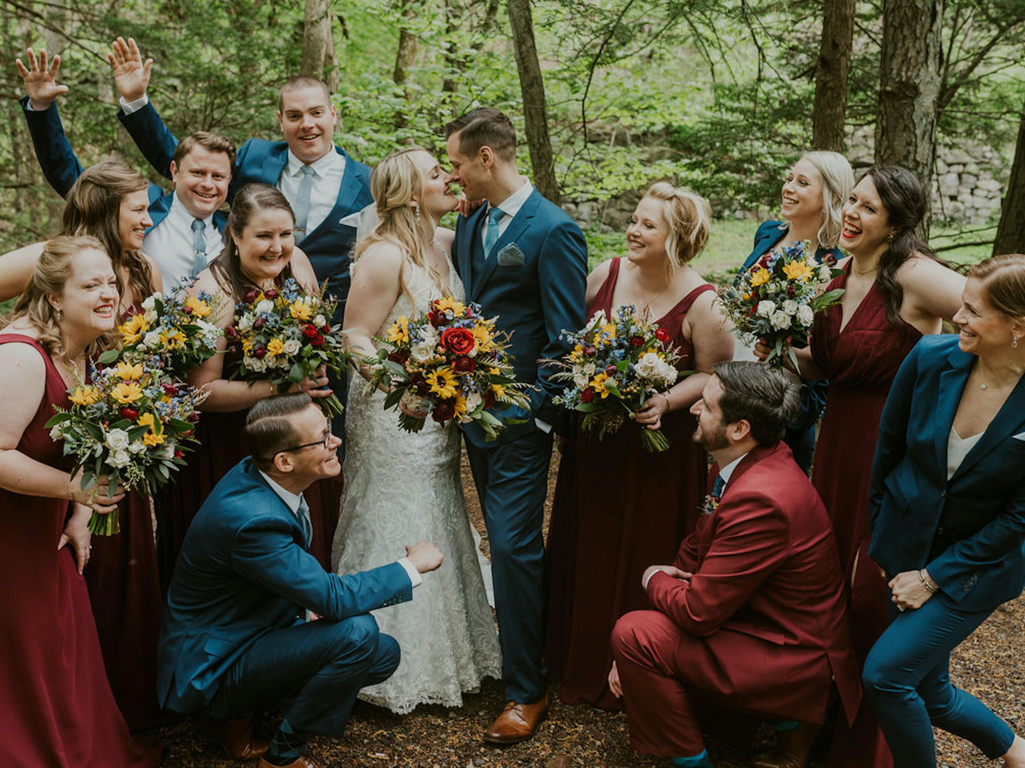 Brilliant Blue suits paired with rustic, deep red bridesmaids dresses. Groomswomen ad groomsmen in coordinating suits