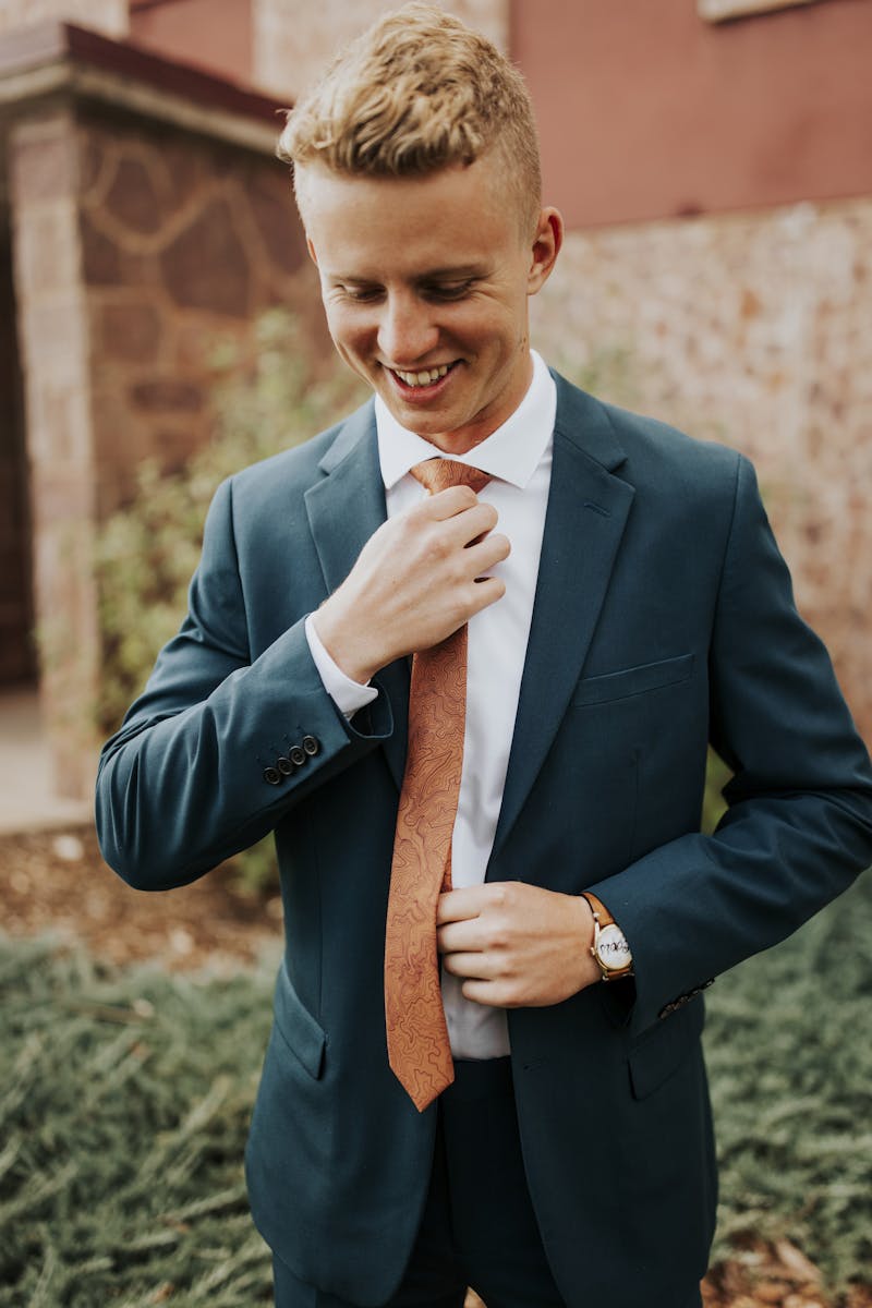 Man tightening his suit tie wearing a green men's blazer and matching green dress pants with orange accessories.
