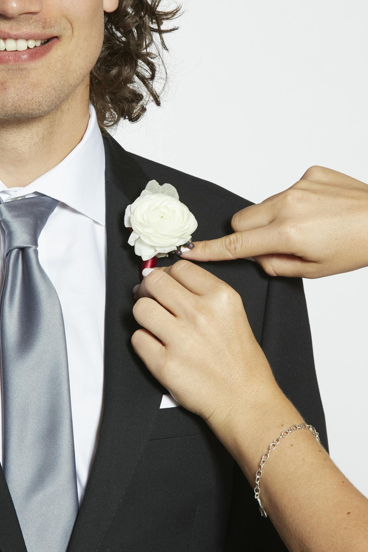 Positioning a white boutonniere on a black suit jacket to pin it in place.