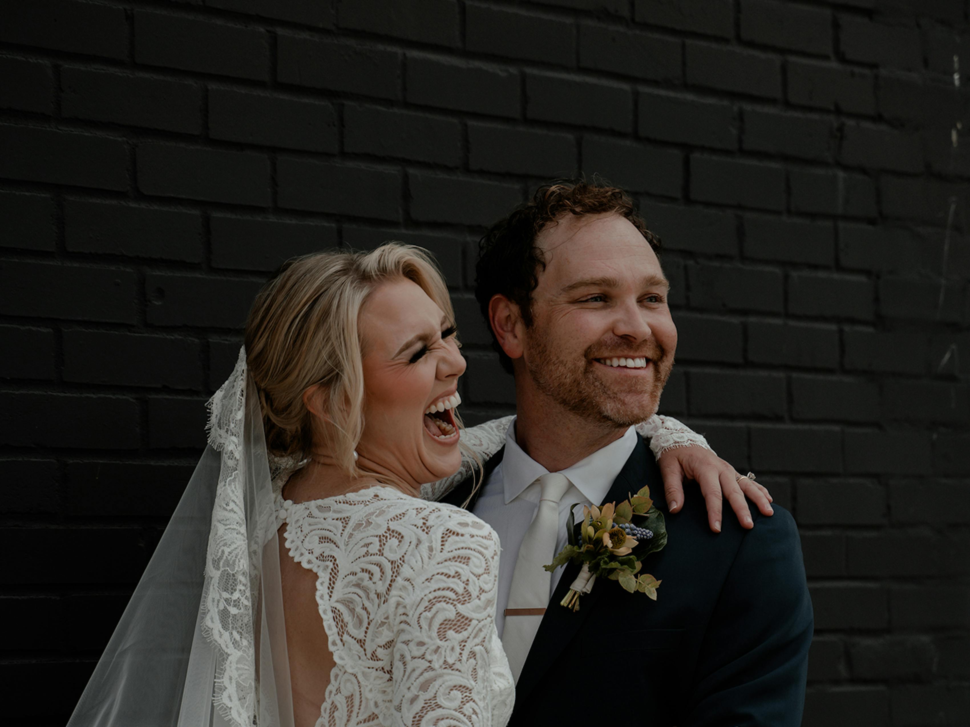 Bride and groom laughing in long sleeve lace wedding dress and dark teal suit with yellow flowers.