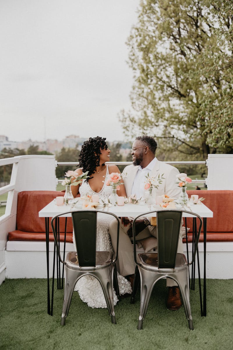 Newlywed table with bride smiling at groom wearing cool suit in tan color