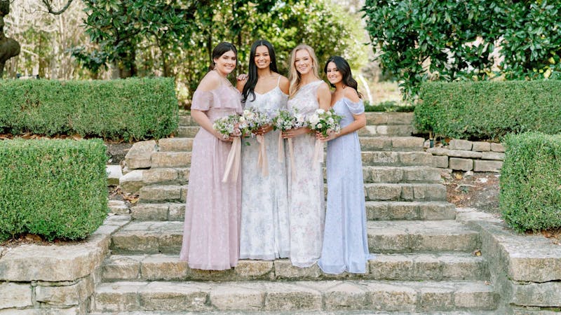 Four bridesmaids in patterned Birdy Grey with a pink floral bridesmaid dress, blue floral, green floral, and white floral at a wedding venue.