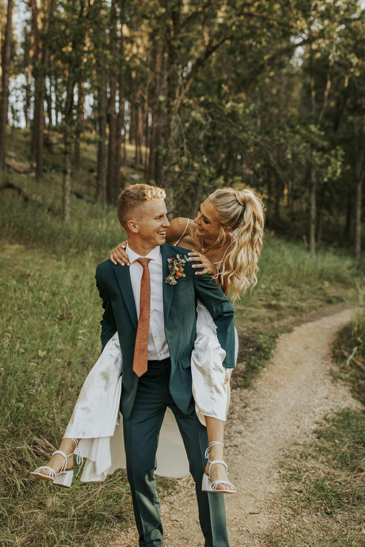 Forest wedding wearing teal wedding suits for grooms in piggyback wedding photo.