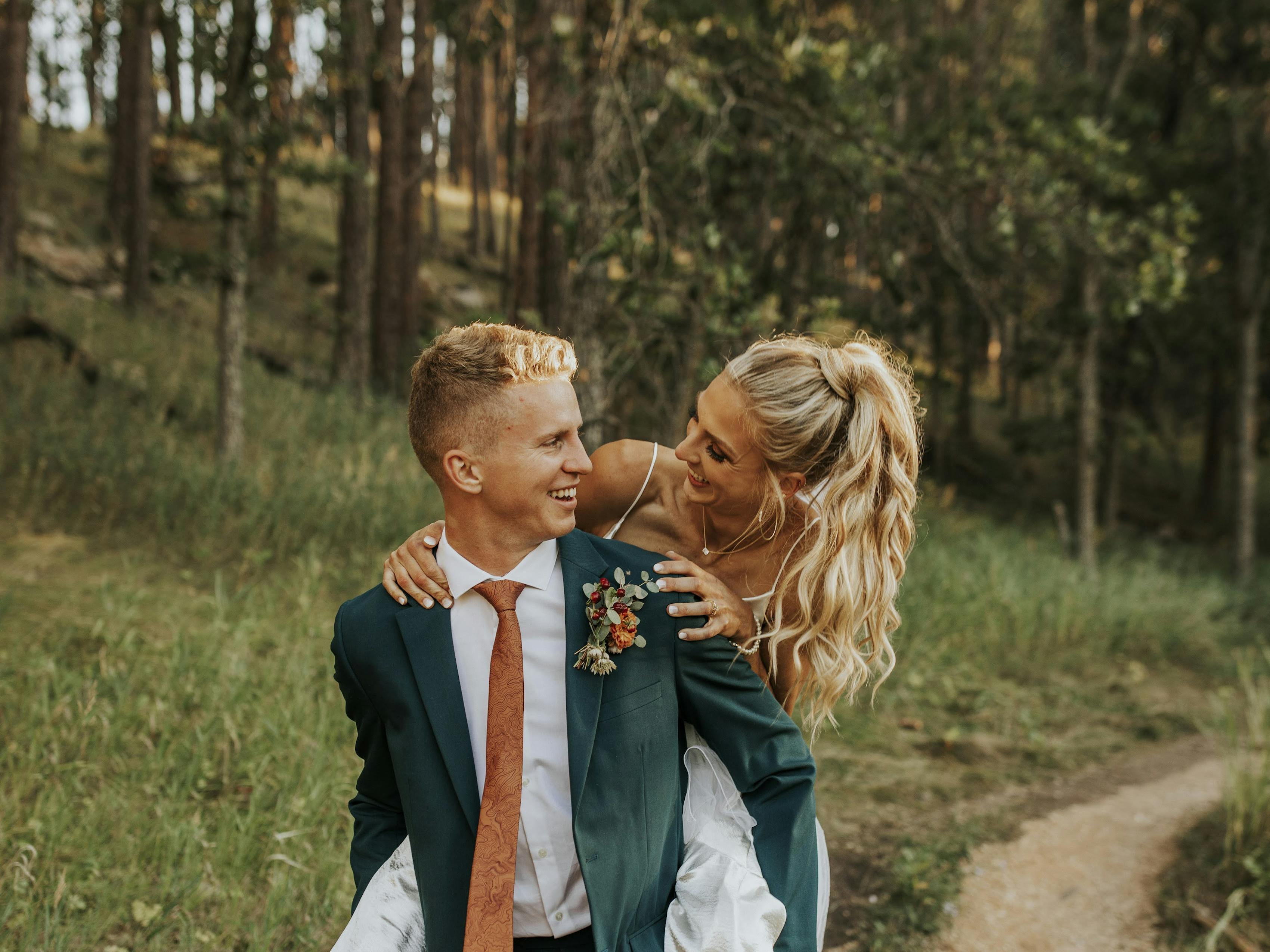 Forest wedding wearing teal wedding suits for grooms in piggyback wedding photo.