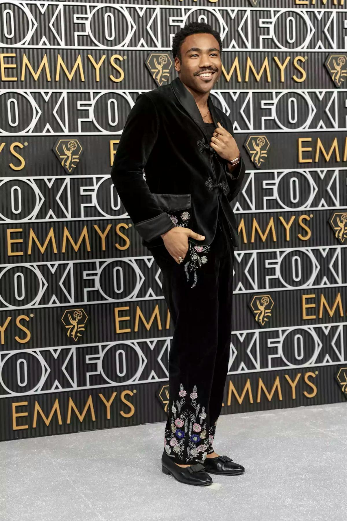Donald Glover 2024 Emmys outfit is a black velvet tuxedo with black satin lapels, embroidered flowers, and patent ballet flats.