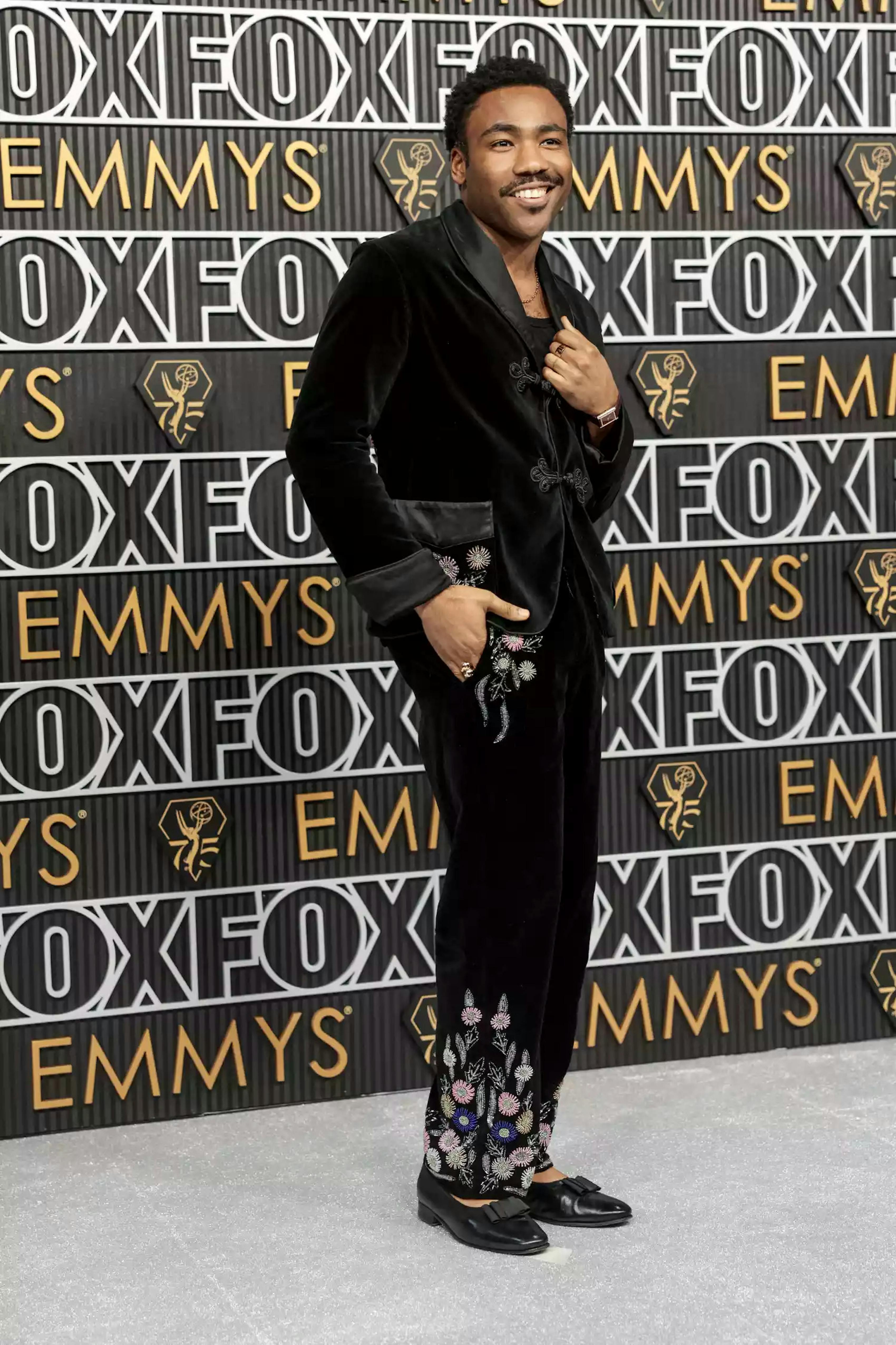 Donald Glover 2024 Emmys outfit is a black velvet tuxedo with black satin lapels, embroidered flowers, and patent ballet flats.