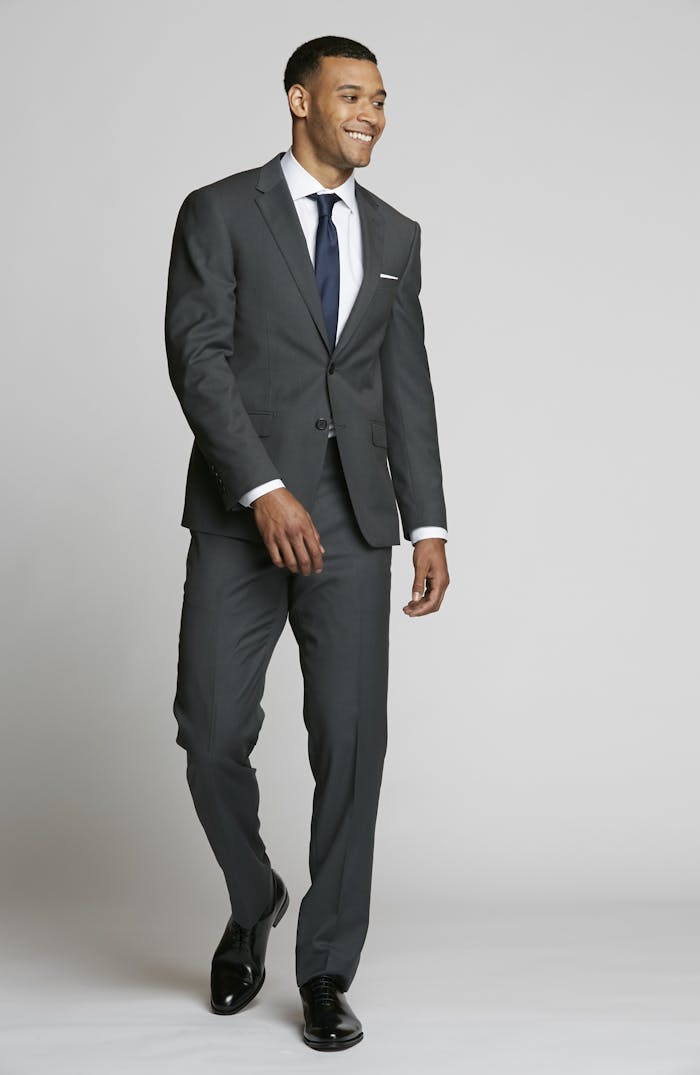 Simple, elegant charcoal grey suit outfit with a white button-up dress shirt and navy tie, perfect to wear as a guest at a formal or cocktail wedding.