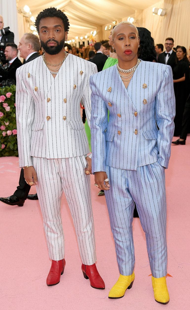 Lena Waithe at the Met Gala in pinstripe double breasted light blue suit and bright yellow shoes.