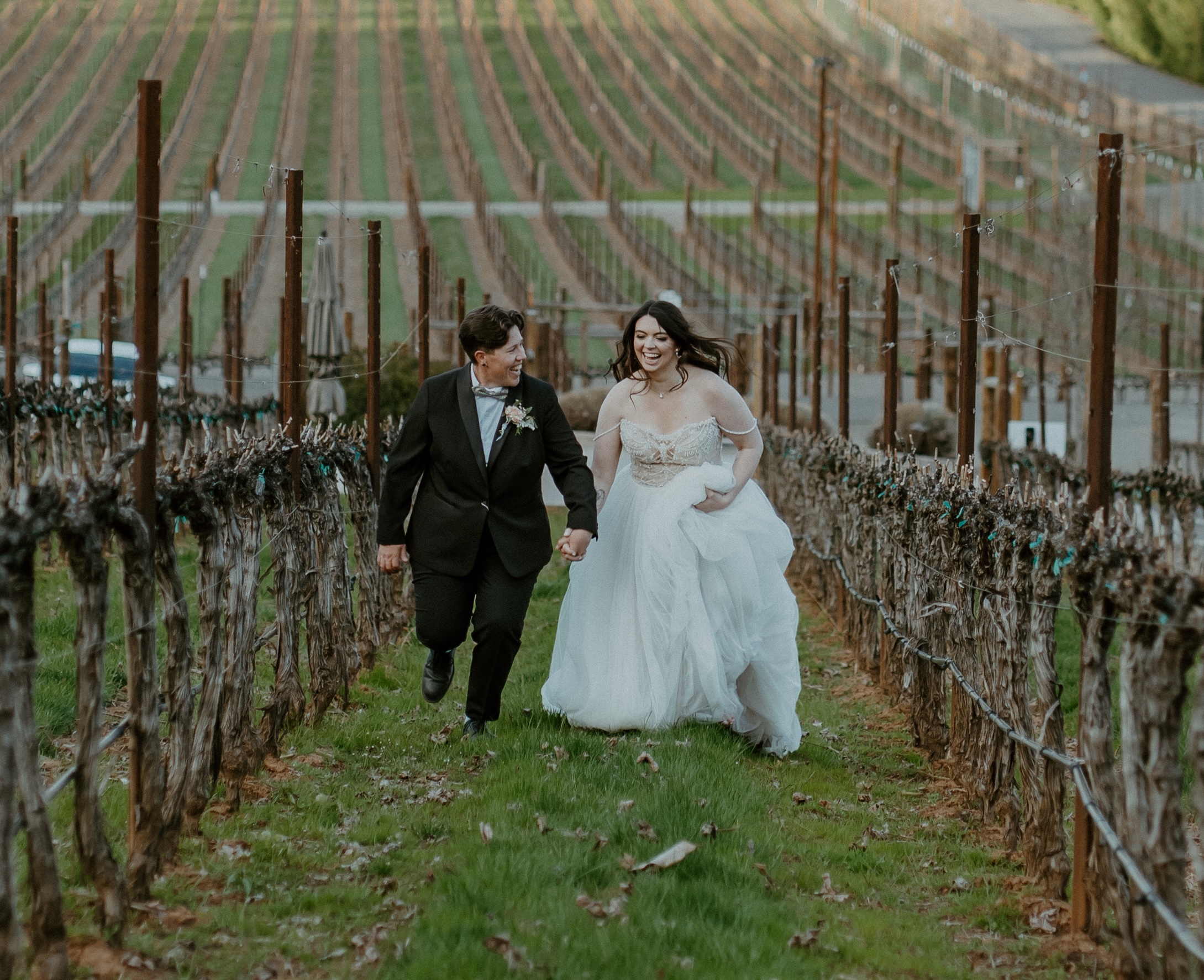 Newlywed couple holding hands while walking through grapevines at a scenic vineyard wedding venue