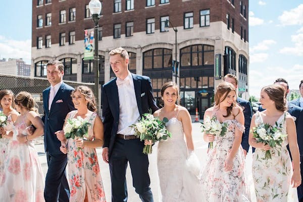 Trendy wedding party in mismatched floral bridesmaid gowns and navy groomsman suits and pink accessories with city background.
