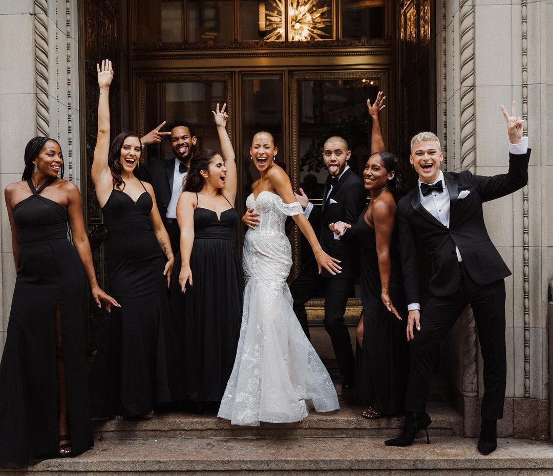 All black bridal party outfit trend and black groomsmen tuxedos for a monochromatic black wedding party celebrating outside the wedding venue.