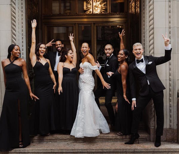 All black bridal party outfit trend and black groomsmen tuxedos for a monochromatic black wedding party celebrating outside the wedding venue.
