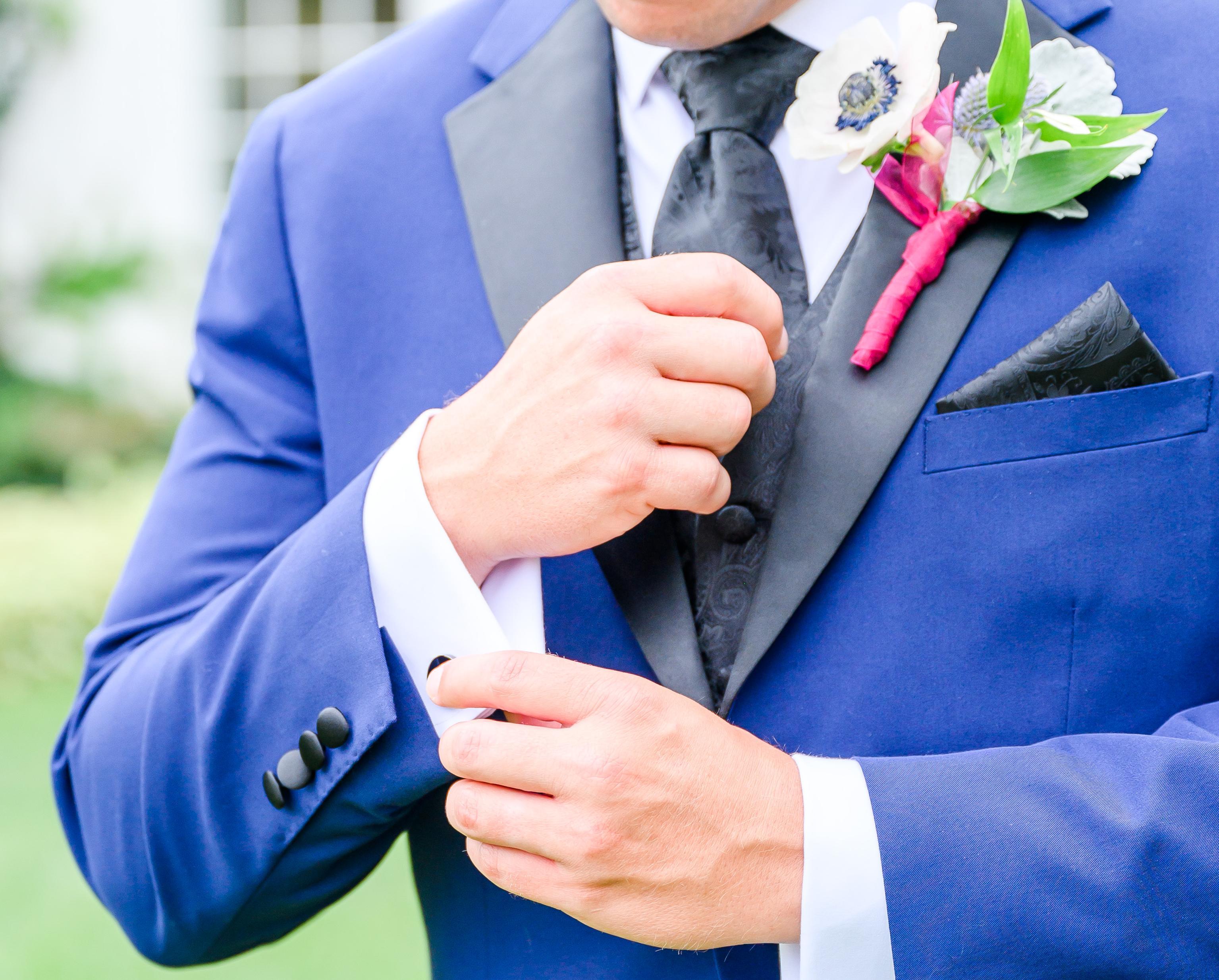 Close-up of a man in a blue tuxxedo with flowers pinned to his lapel and a black patterned tie.