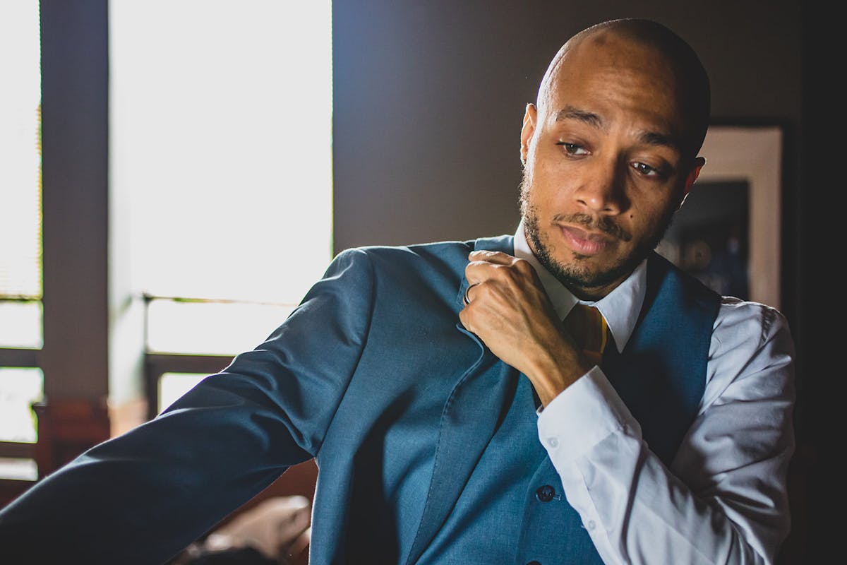 Man getting dressed in a blue blazer with a matching blue suit vest.