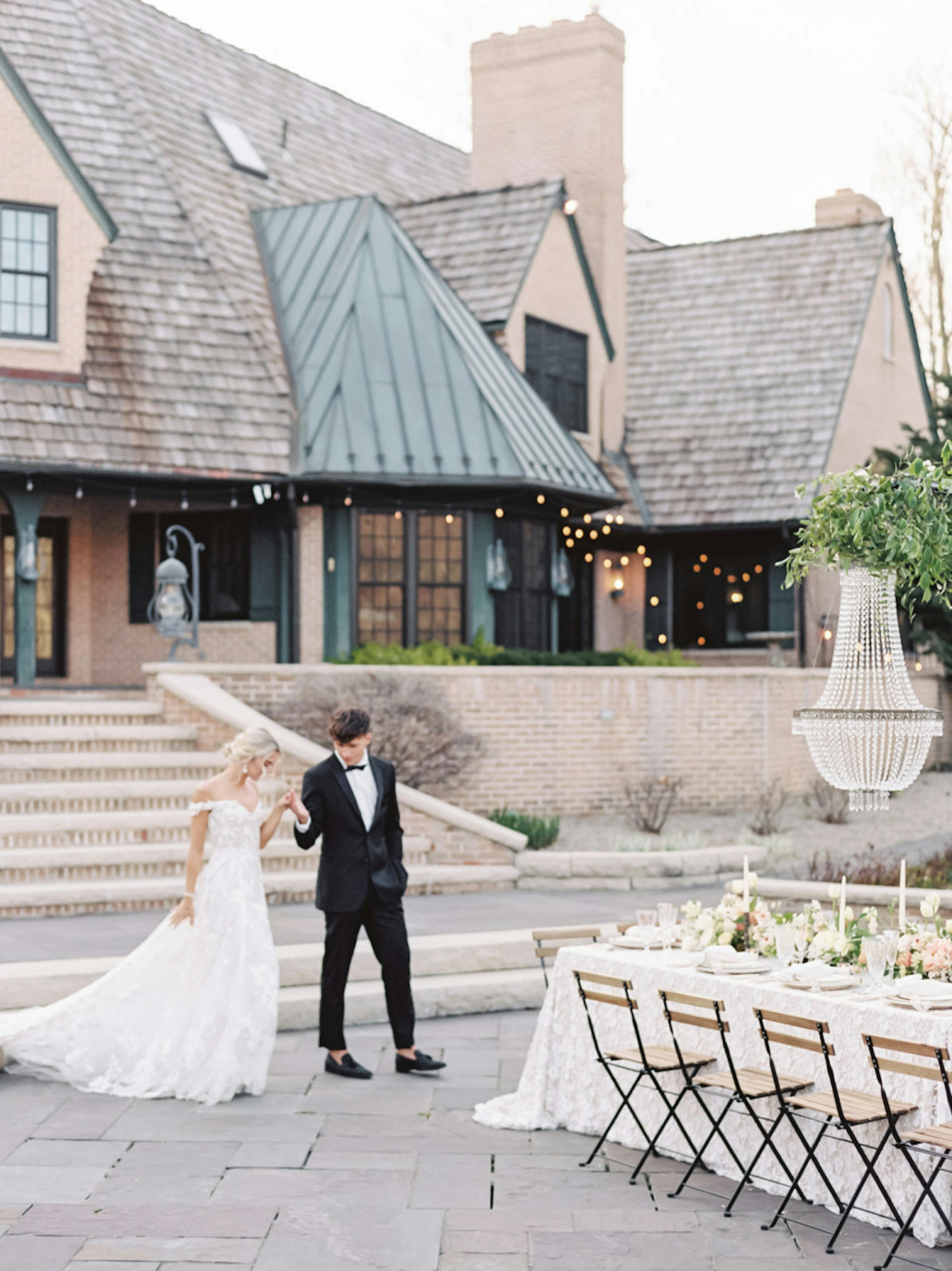 Groom wearing timeless black tuxedo for wedding and loafers guiding bride by the hand at European destination style venue.