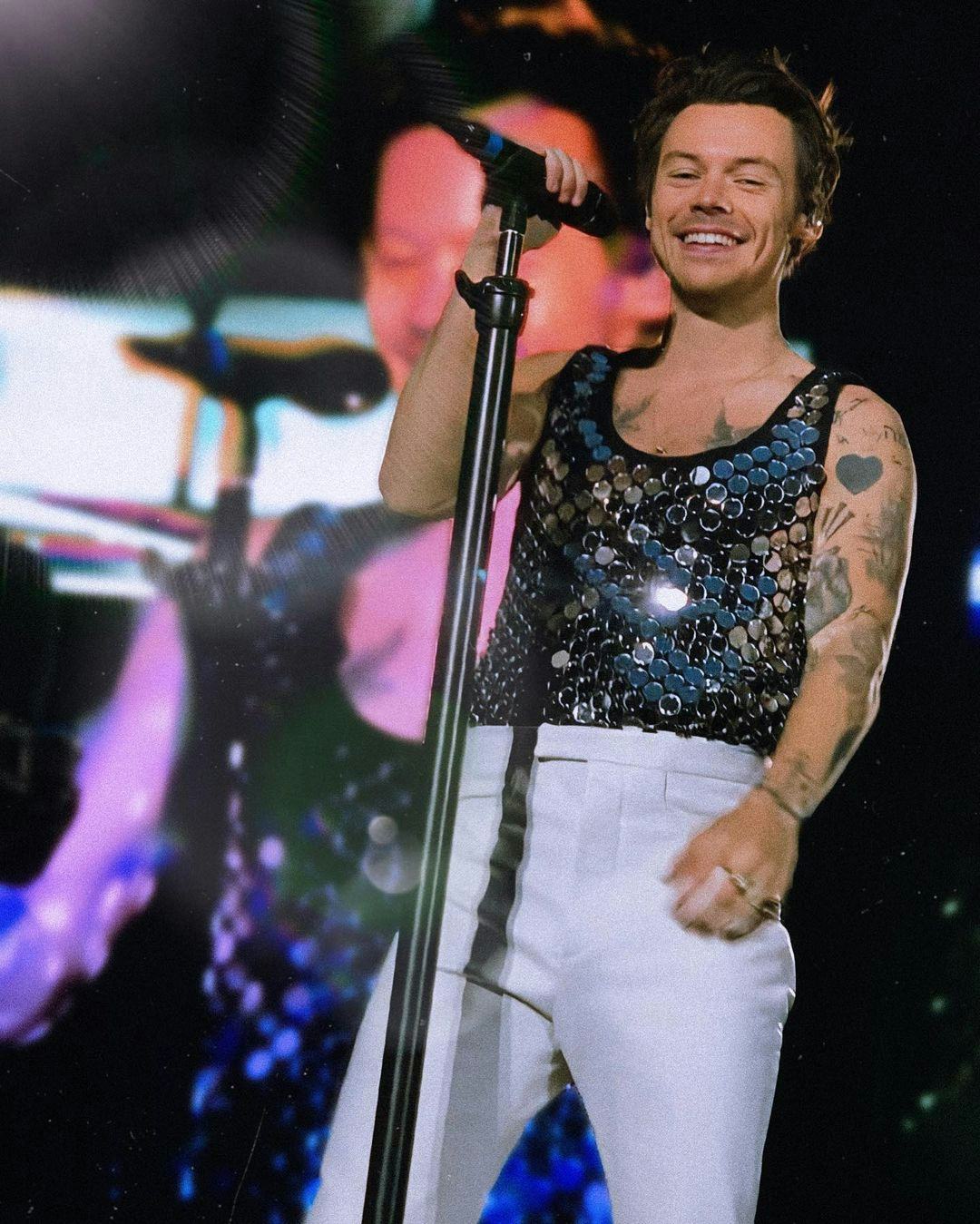 Harry Styles in sequin top and white suit pants performing on stage live at Wembley Stadium for Love on Tour concert.