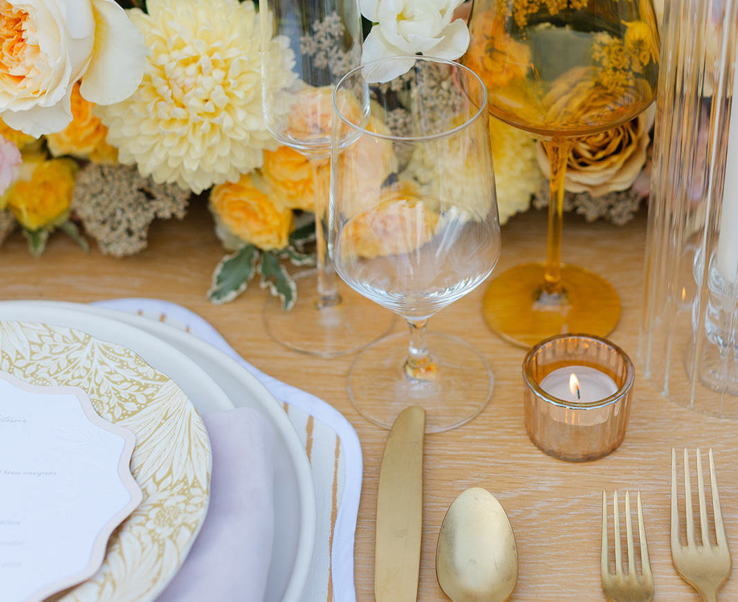 Elegant wedding table setting with gold flatware, glassware, candles, floral arrangements, and decorative plates.