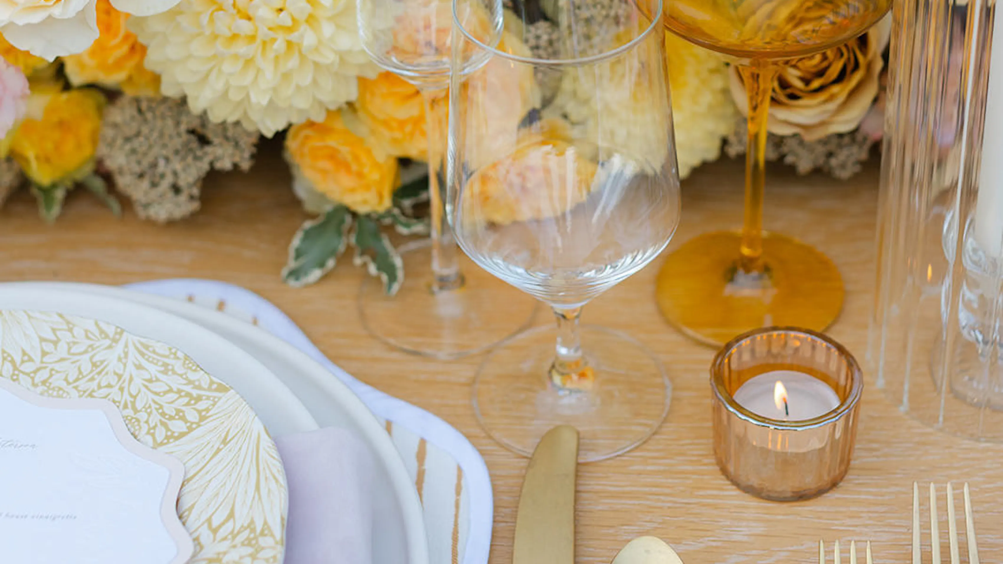 Elegant wedding table setting with gold flatware, glassware, candles, floral arrangements, and decorative plates.