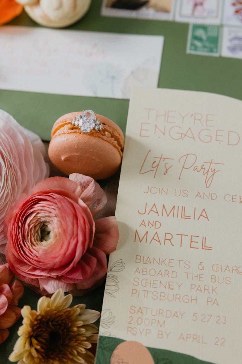 Wedding dessert macaron with engagement ring, flowers, and wedding invitation for pink, yellow, orange, tan, and white neutral wedding color palette with bright pops