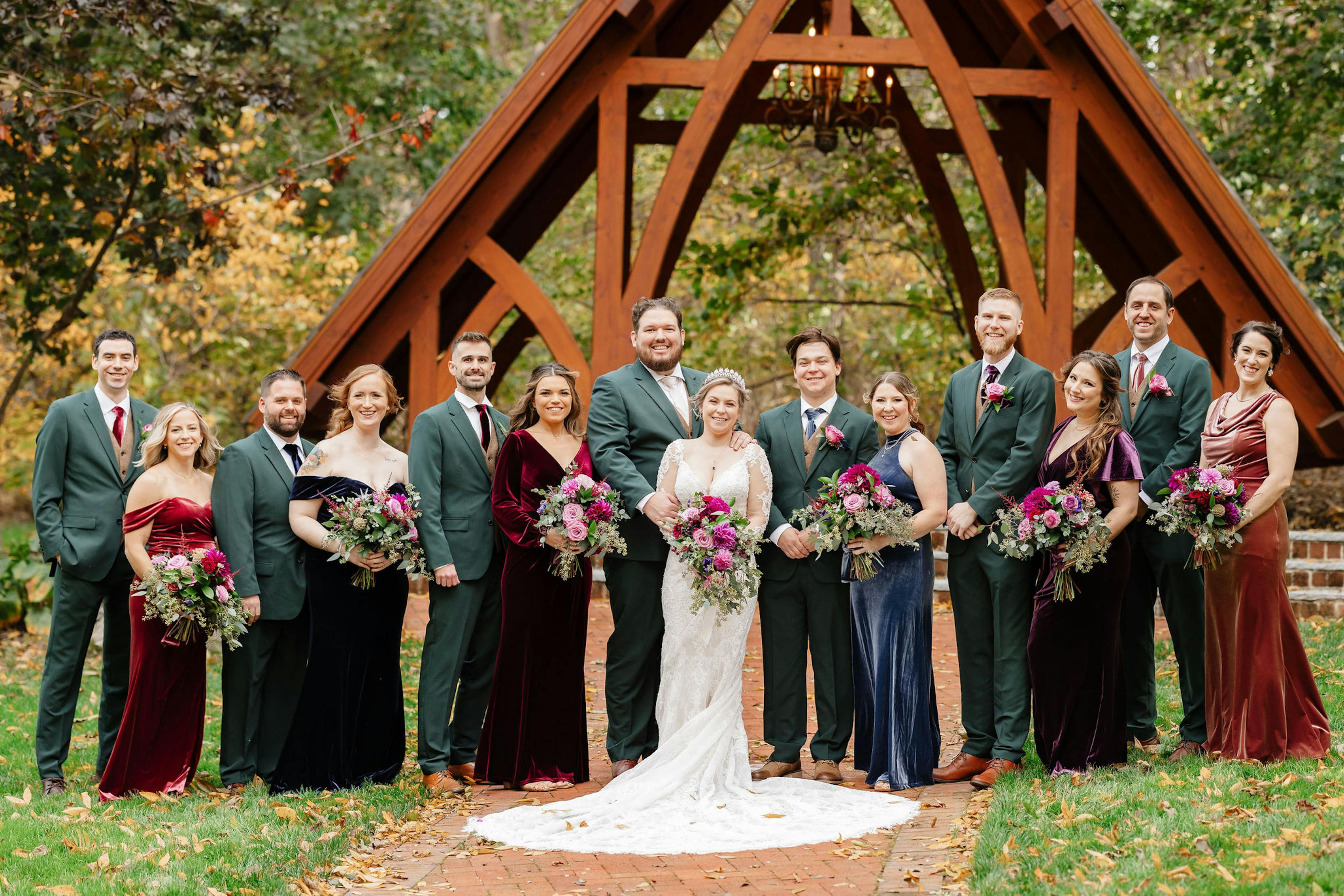 Fall colors wedding party in velvet mix and match bridesmaids dresses and forest green groomsman suits.