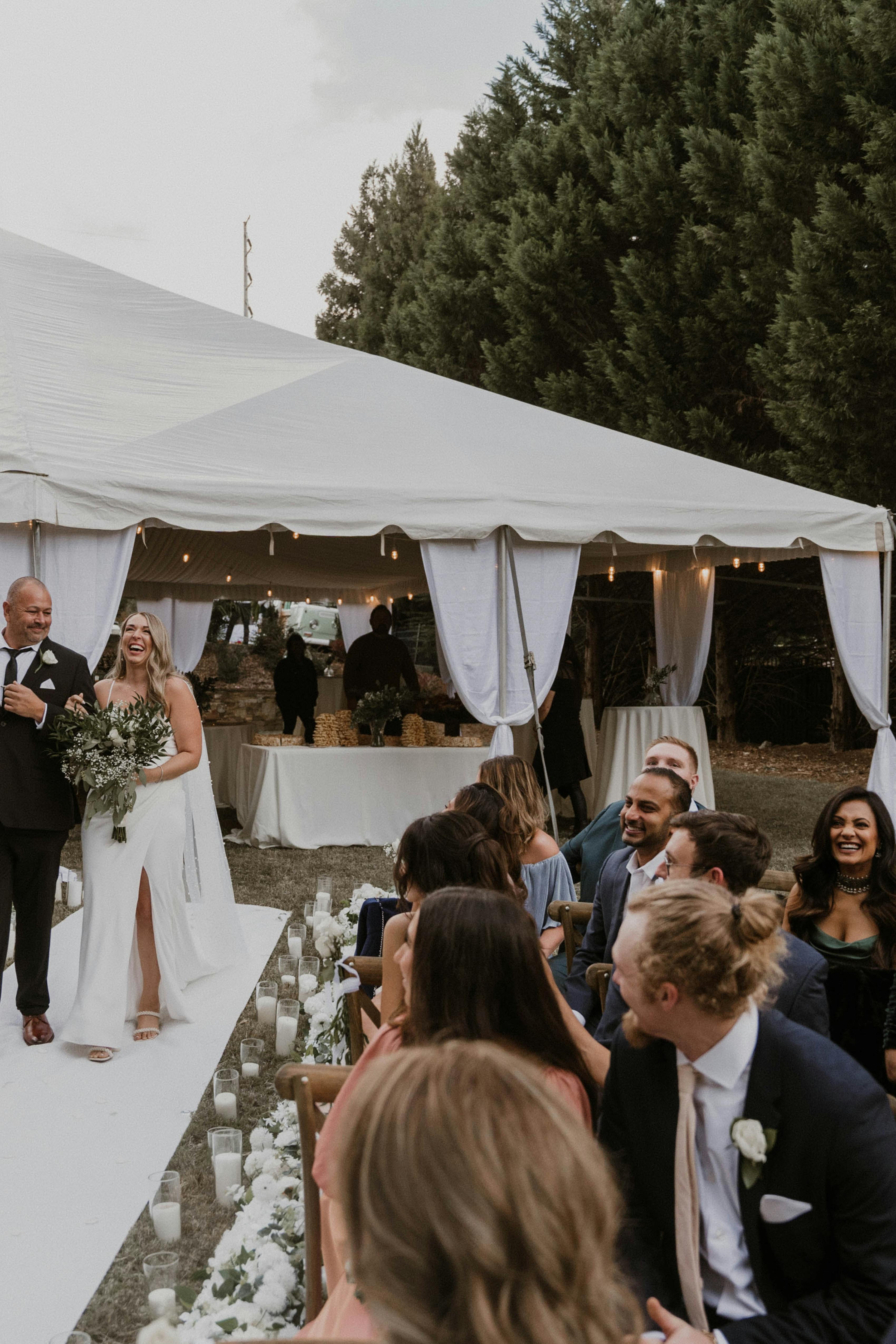 Father of the bride walking down the aisle in black suit for weddings with brown shoes in backyard neutral wedding.