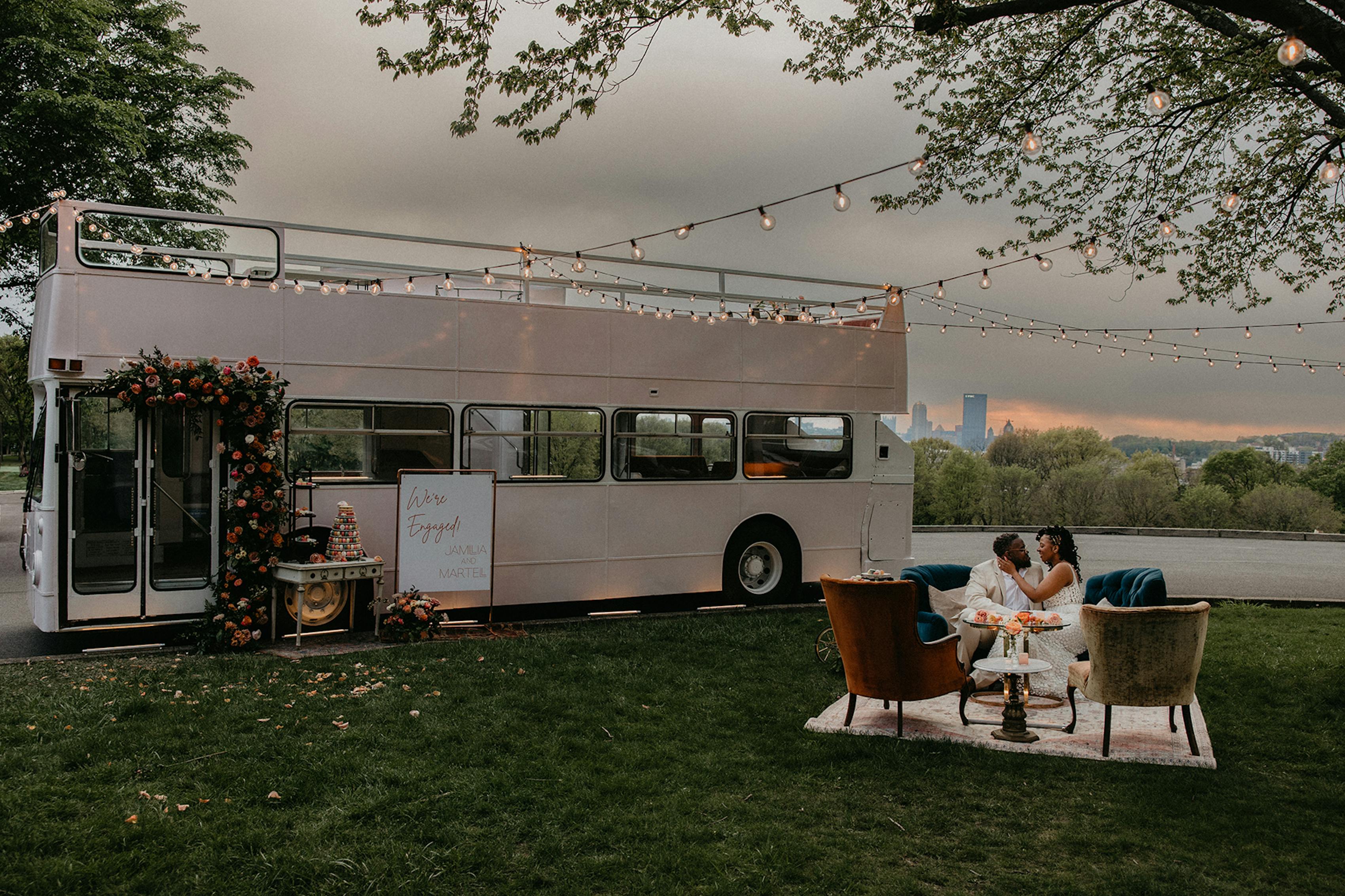Bride and groom hugging wearing neutral light and airy wedding attire in front of double decker bus venue in city park.