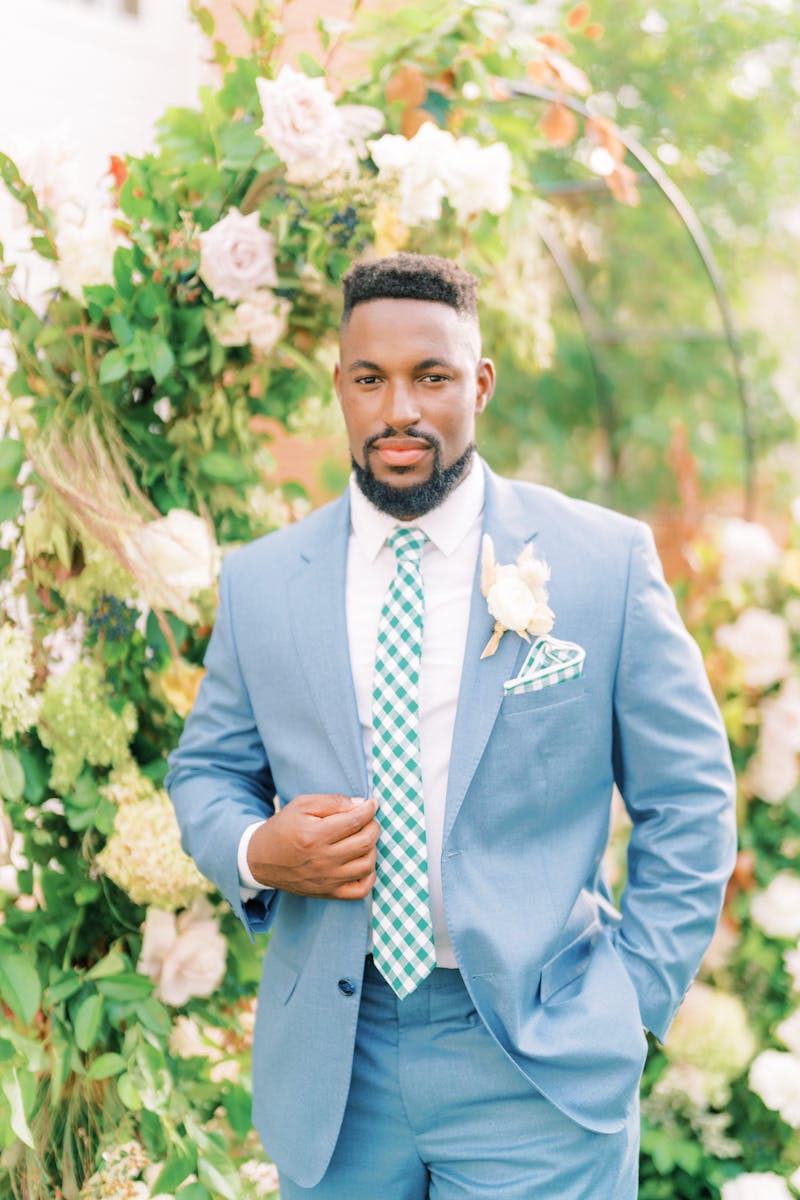 Man wearing pastel preppy suit style for summer with light blue suit and green gingham tie and matching pocket square in garden.