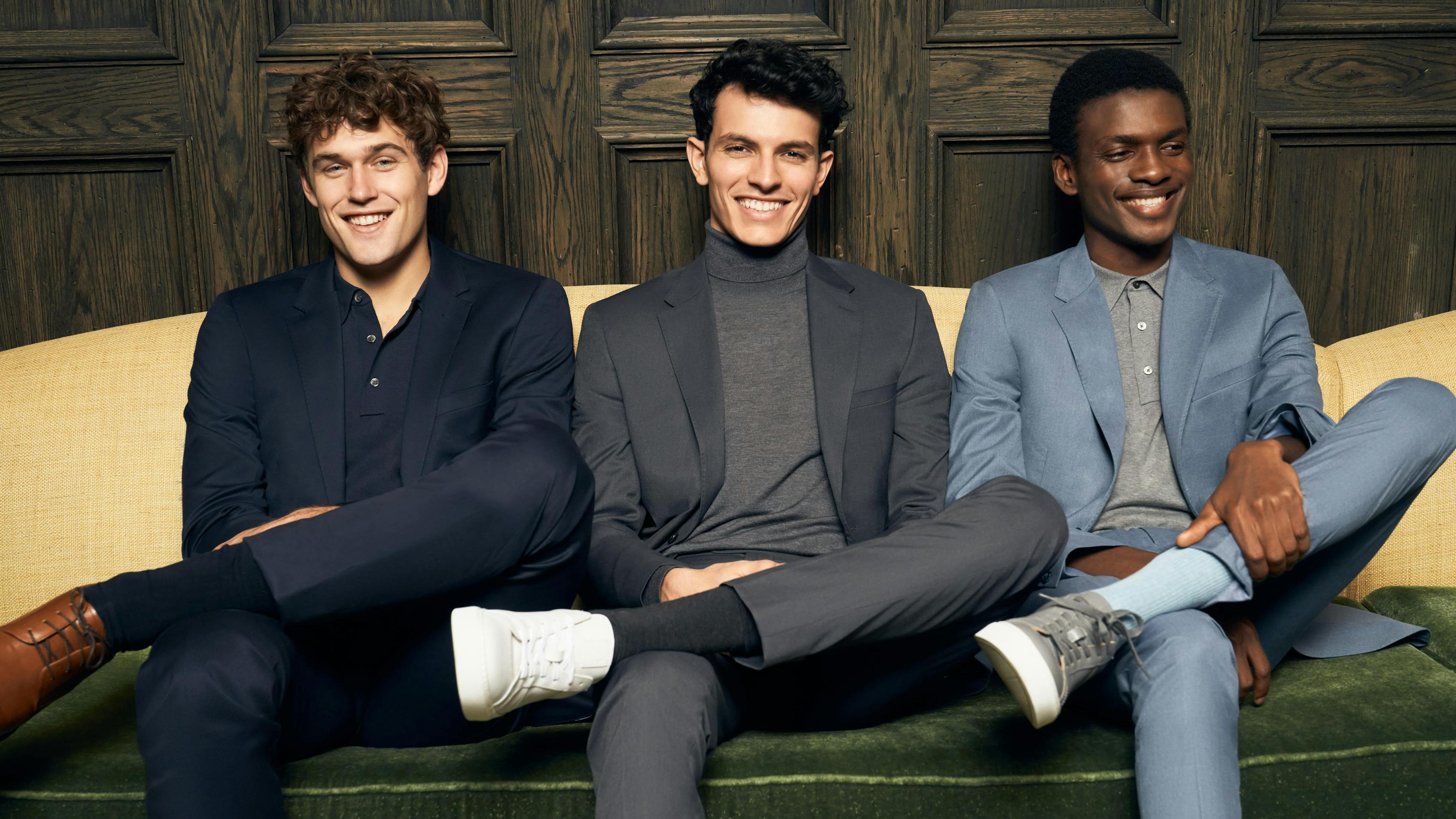 Three men dressed for the office in smart casual outfits for work, including a monochromatic men's navy suit, dark grey suit for men, and a professional light blue suit.
