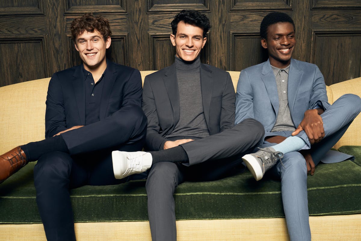 Three men dressed for the office in smart casual outfits for work, including a monochromatic men's navy suit, dark grey suit for men, and a professional light blue suit.