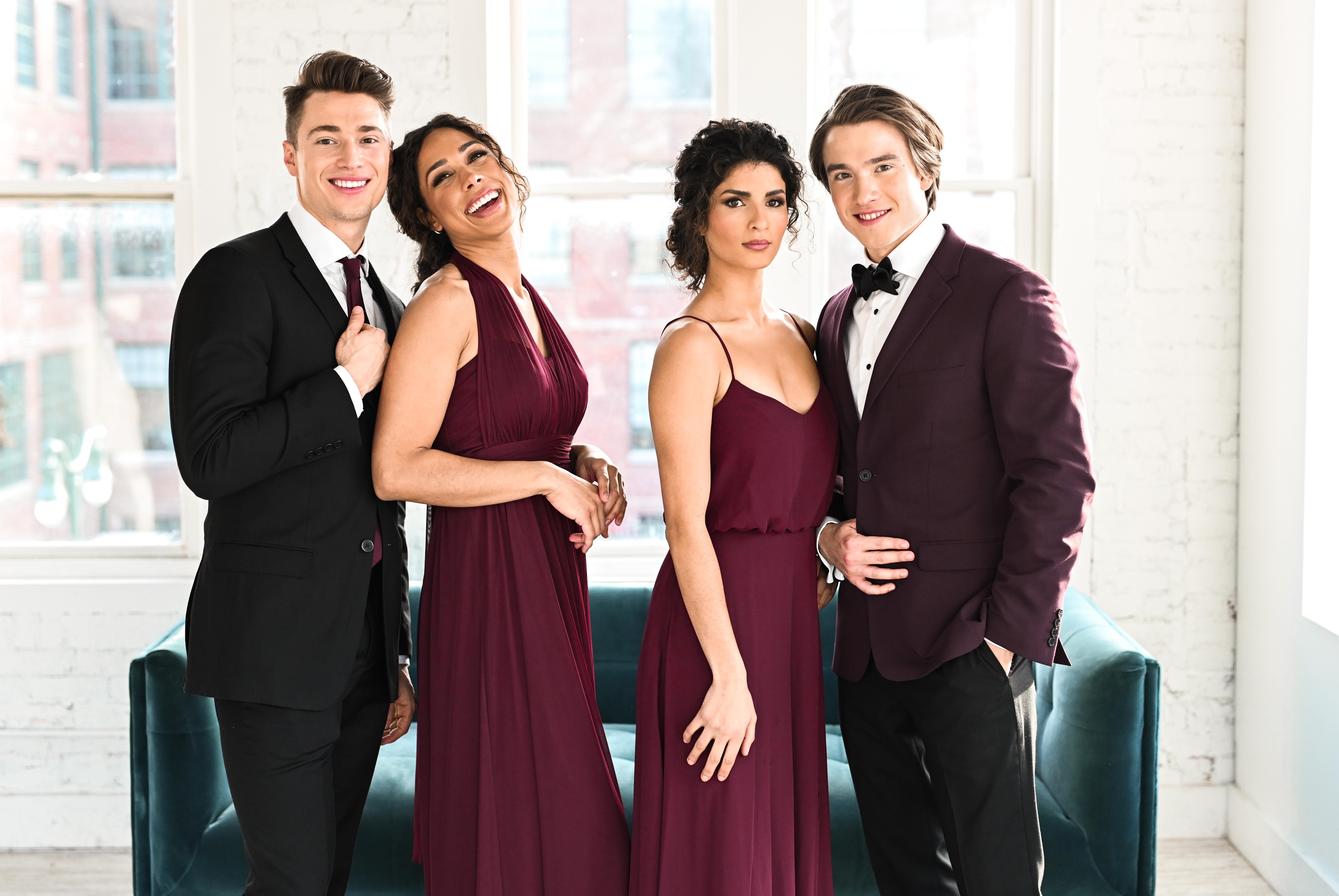 Four winter wedding guests posing in coordinated burgundy outfits, including two formal dresses, a black suit, and a burgundy tuxedo jacket.