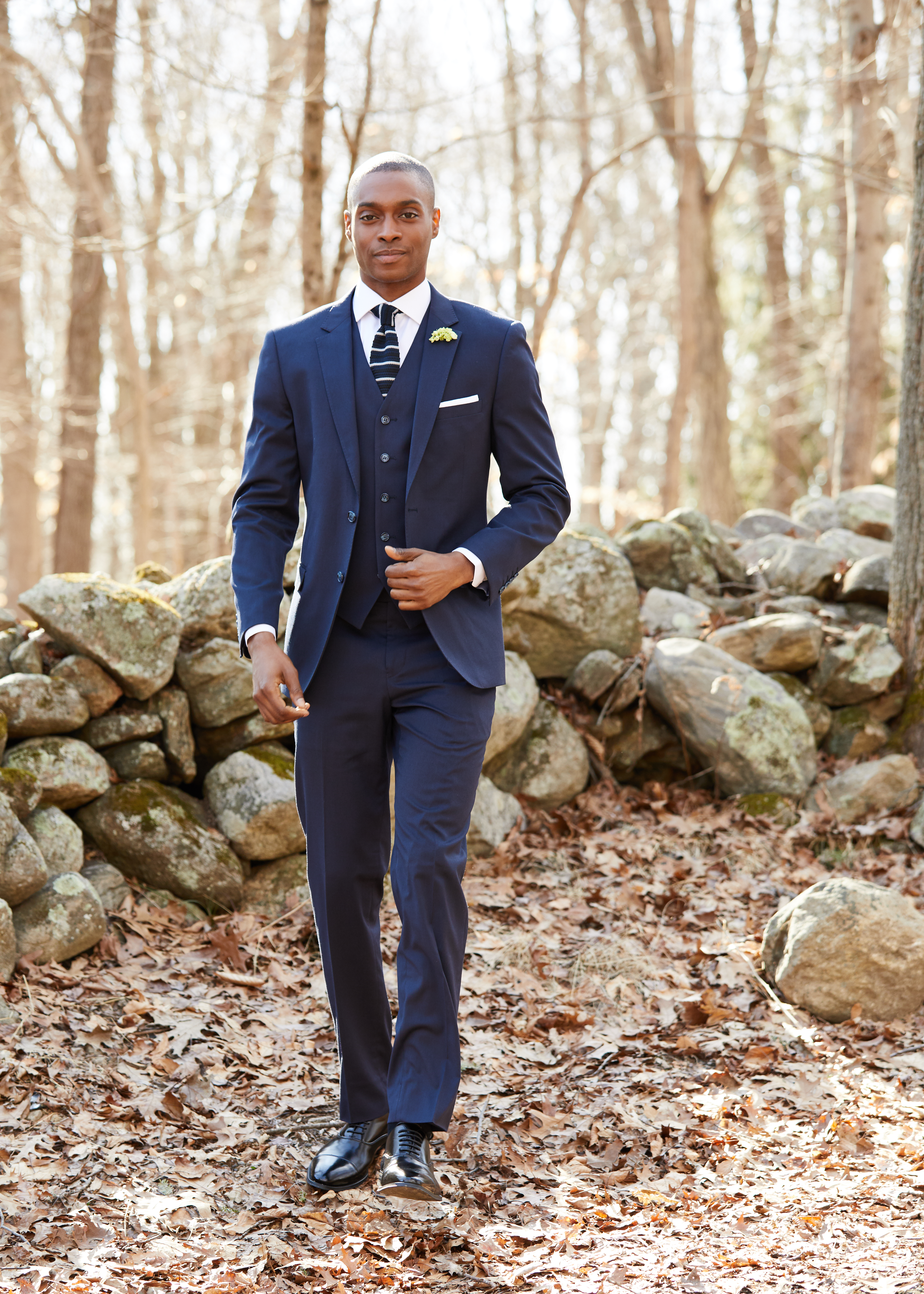Man wearing a navy three-piece suit with a striped tie at an outdoor fall wedding.