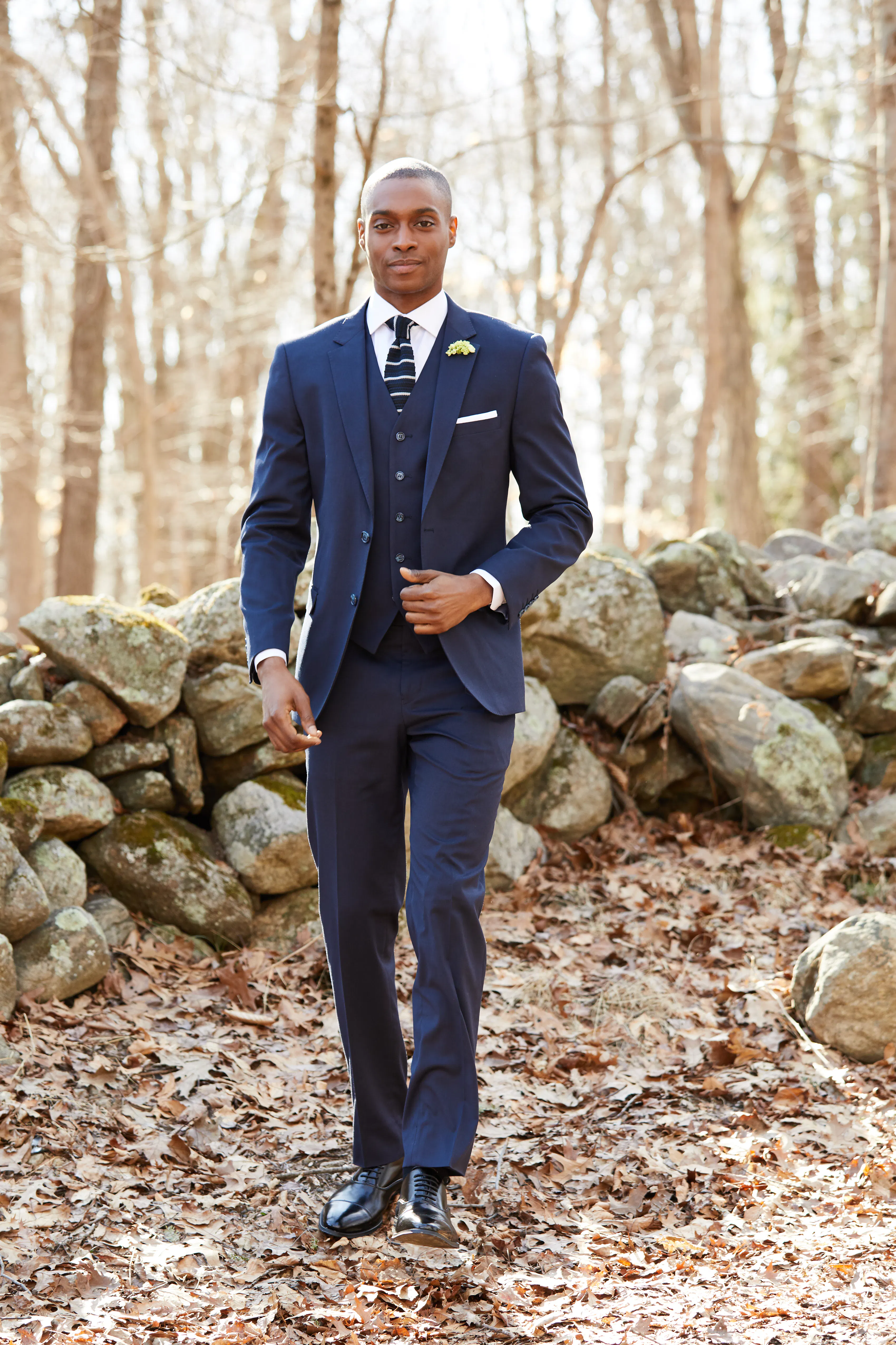 Man wearing a navy three-piece suit with a striped tie at an outdoor fall wedding.