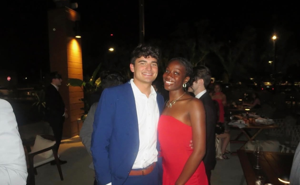 Couple posing together at a fraternity formal, with the man wearing a royal blue suit and white shirt and the woman in a strapless red dress.