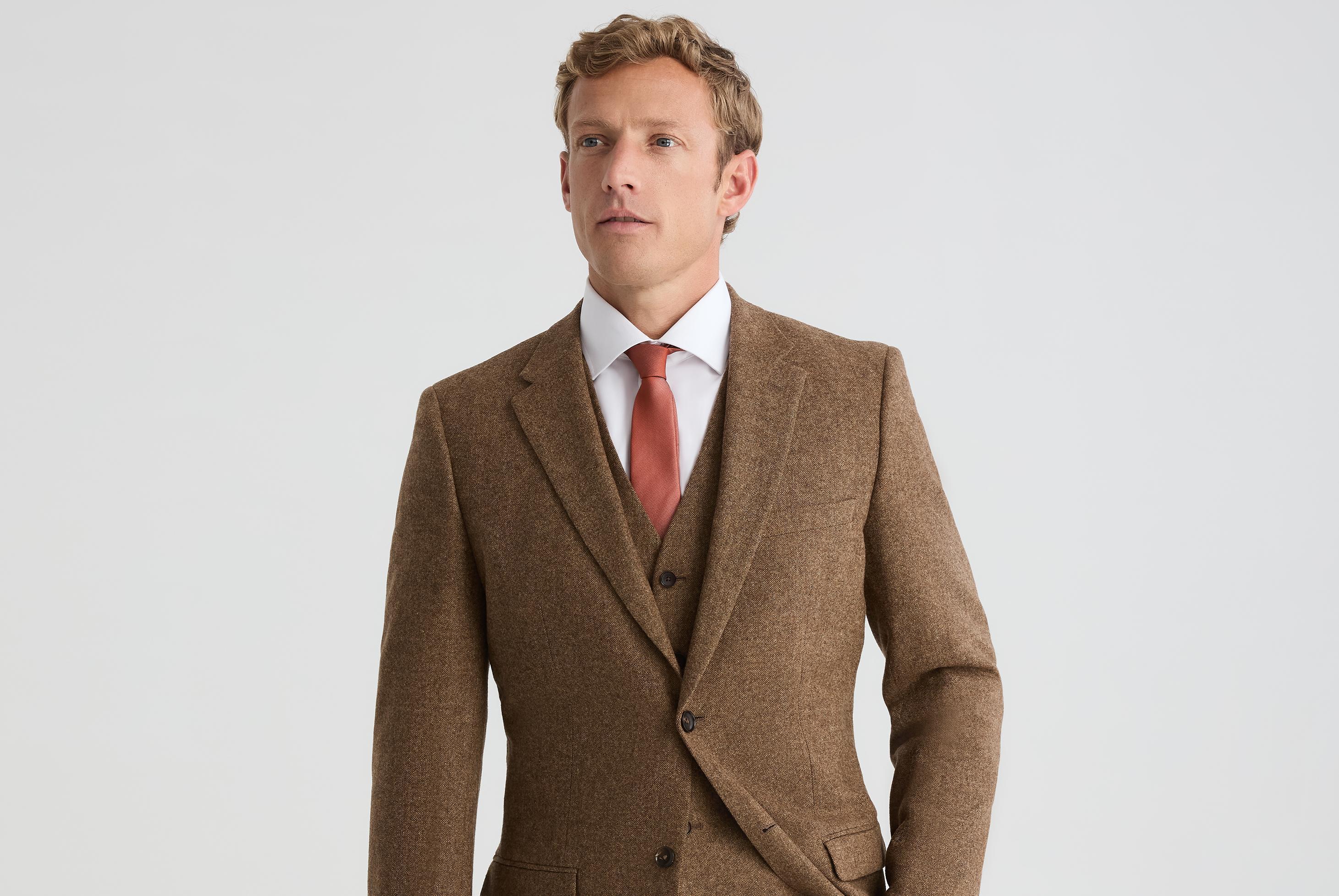 Man wearing a brown three-piece suit with a white dress shirt and rust-colored tie for a fall wedding look.
